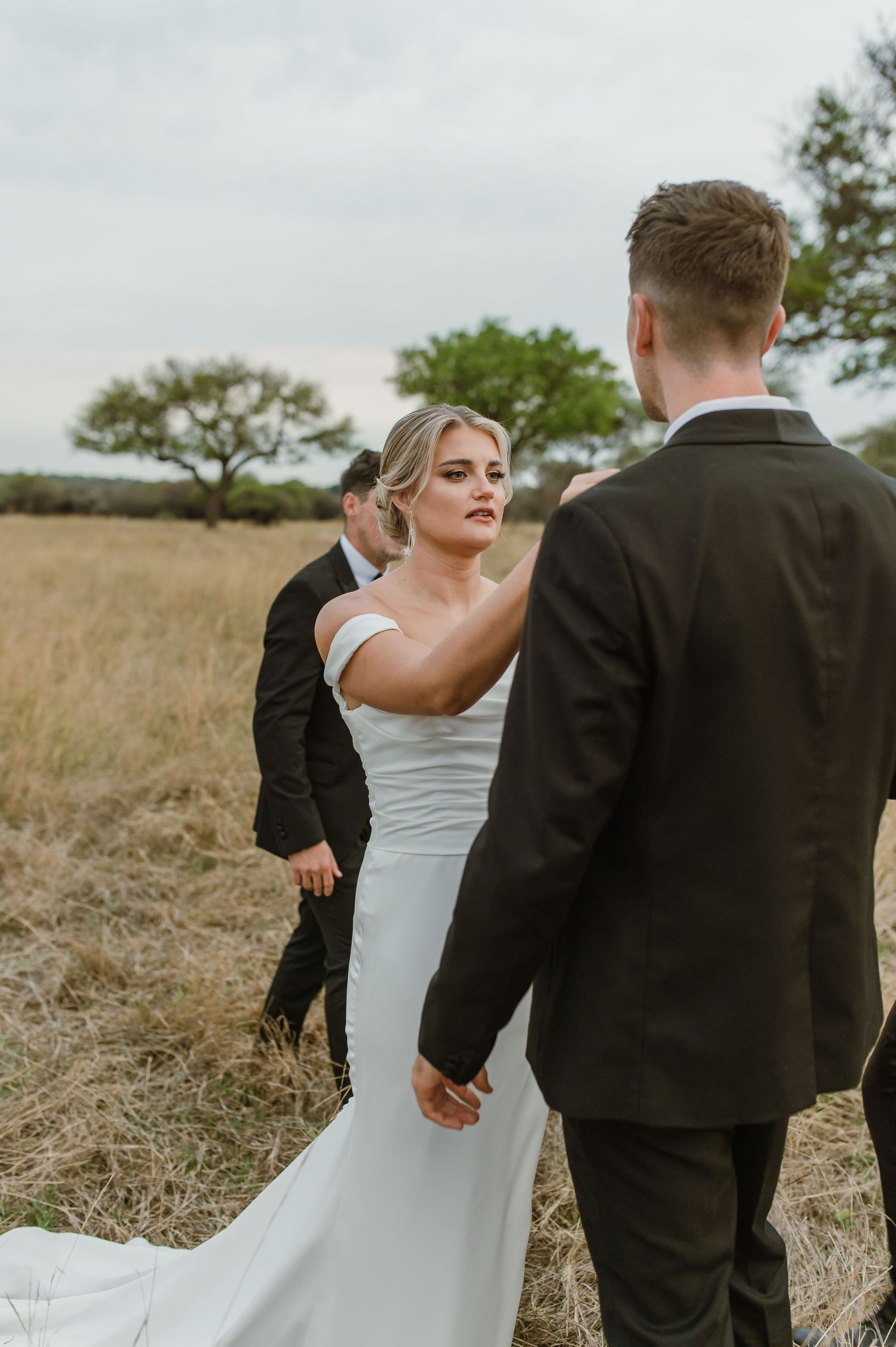 Wedding party members playfully pose together in a golden field during sunset.