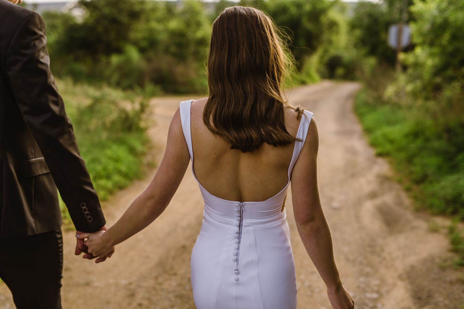Back view of a couple walking down a scenic country path during their wedding.