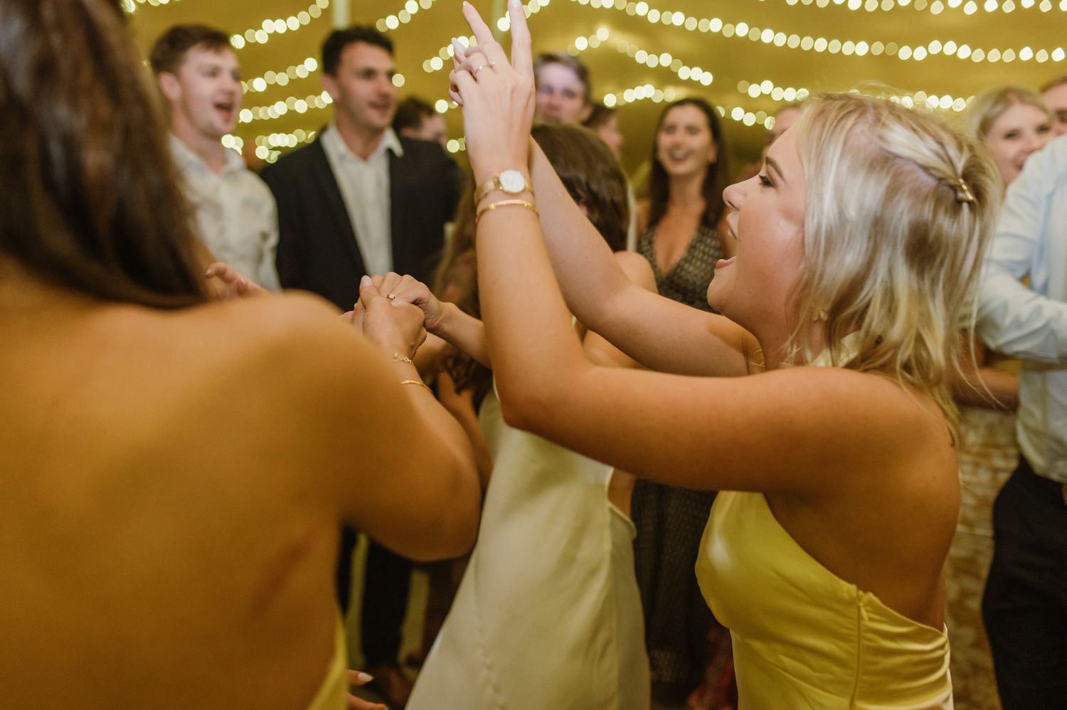 Festive wedding reception with string lights illuminating guests dancing and celebrating.