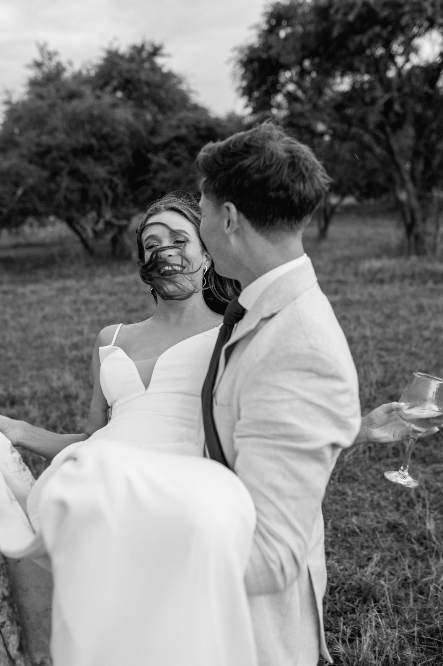 A black and white capture of a wedding couple sharing laughter while the groom carries the bride.