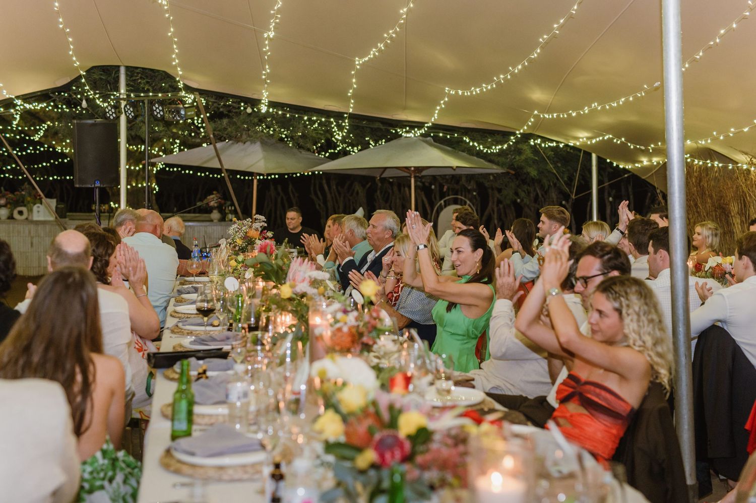 String lights create a romantic canopy over an outdoor wedding reception with decorated dining tables.