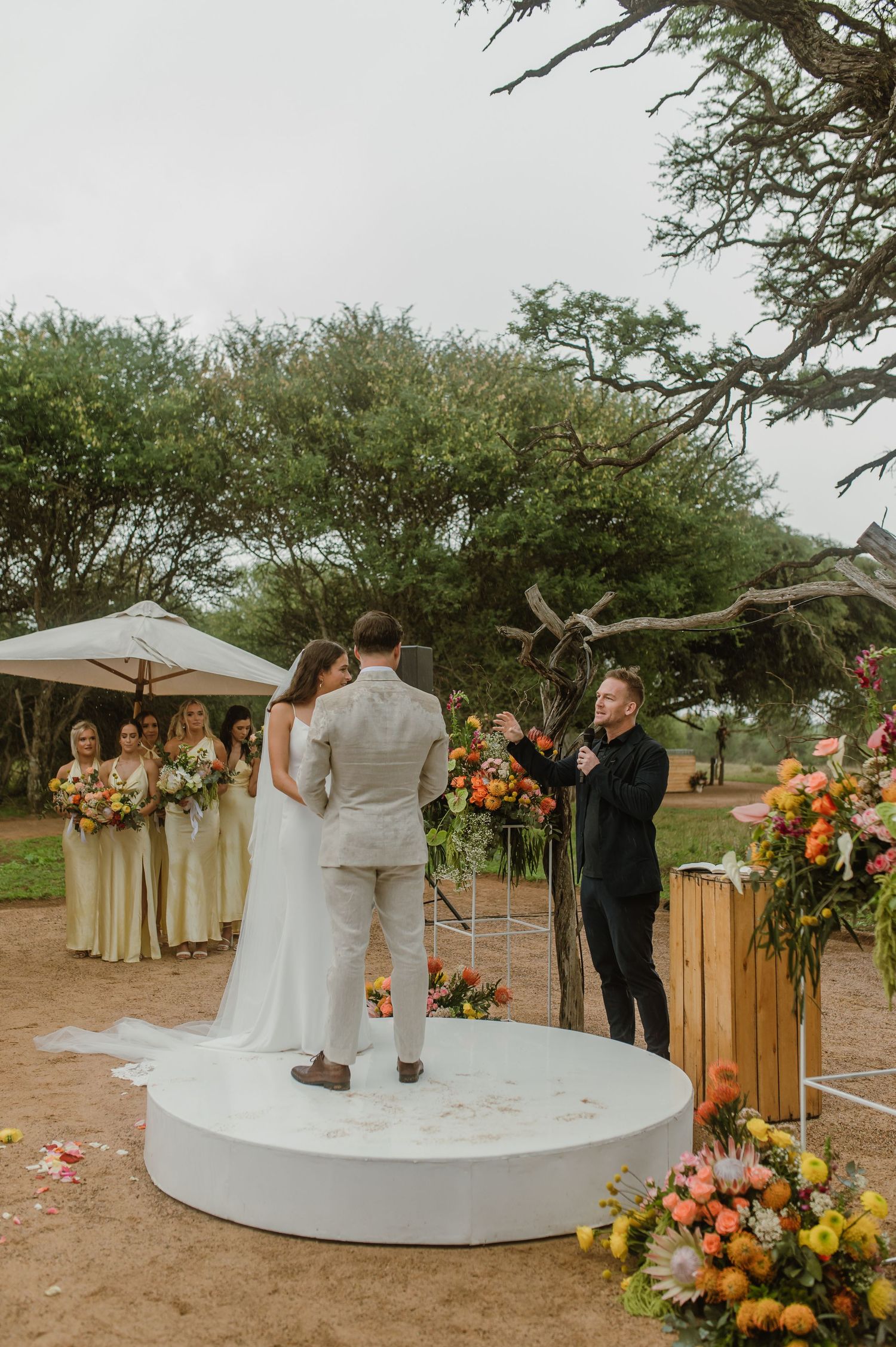 A wedding ceremony on a white circular platform with bright floral arrangements and desert scenery.