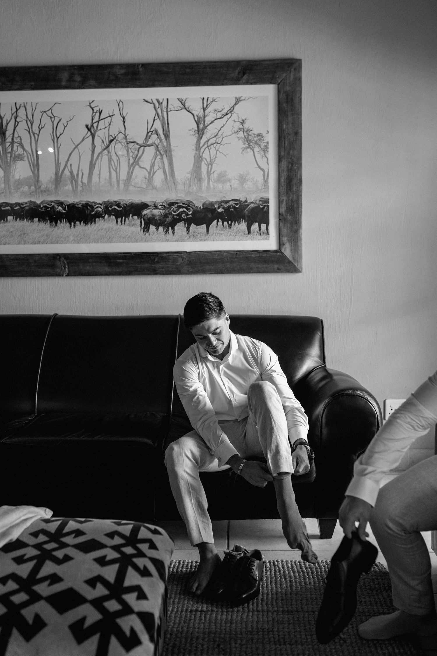 Black and white image of people getting ready in room with framed landscape artwork.