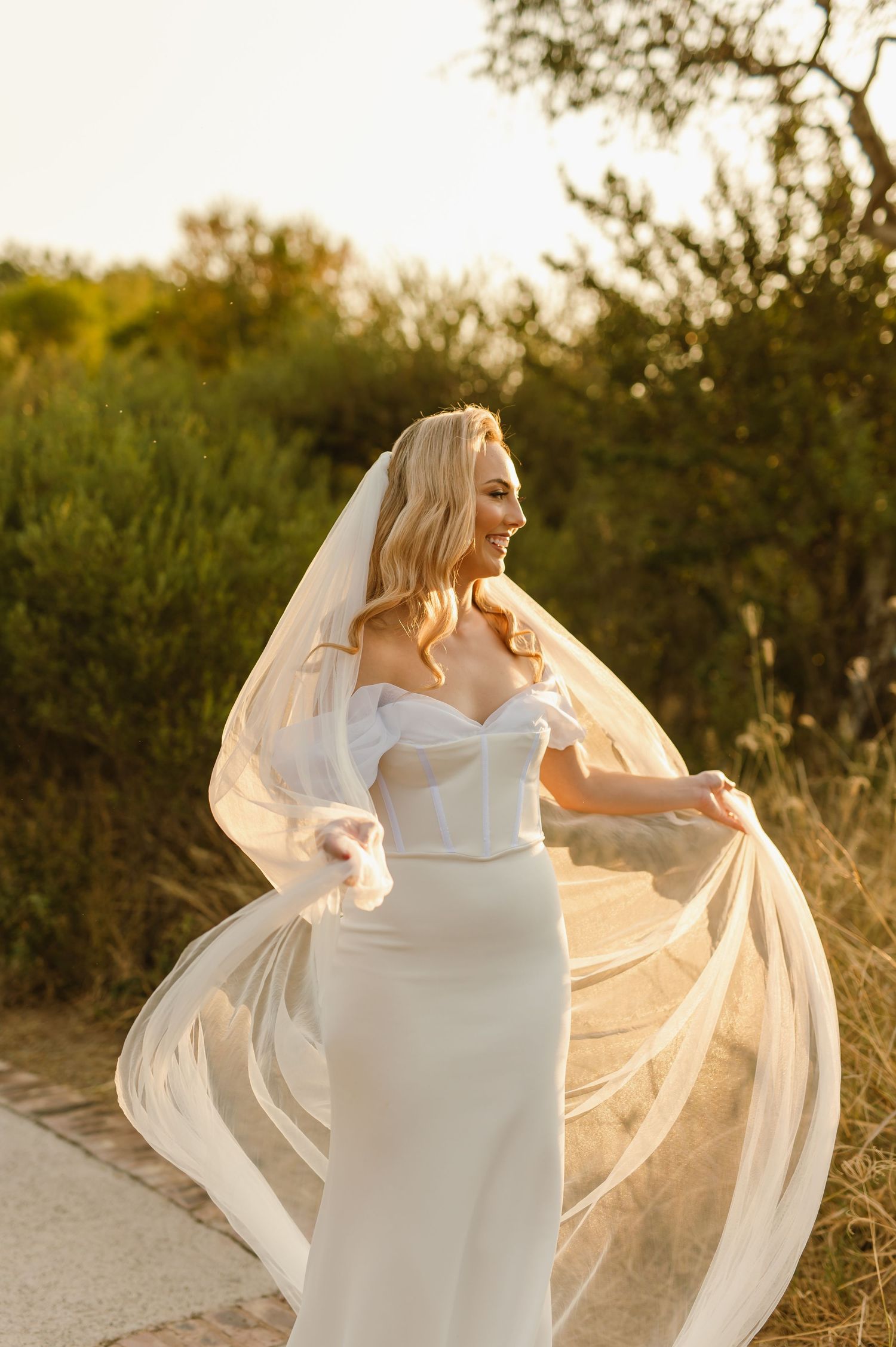 Bride twirls in white wedding dress as sunlight creates a golden glow through her veil.