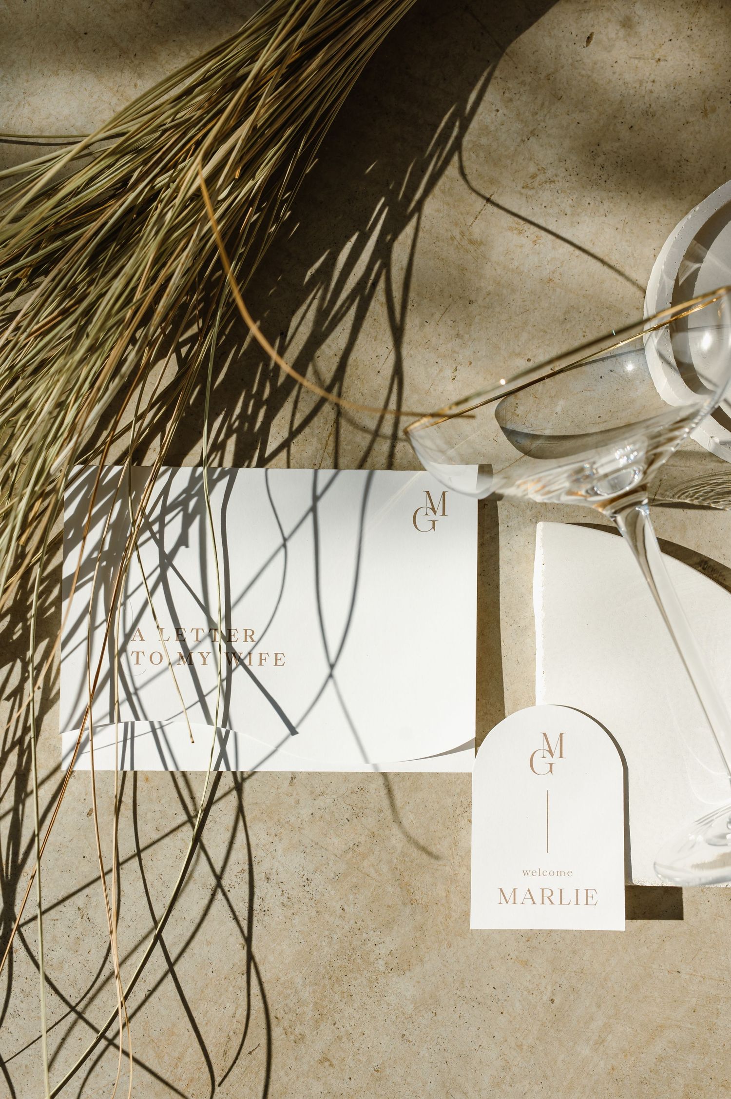 Rustic wedding name cards hanging with dried wheat stalks creating natural decor element.