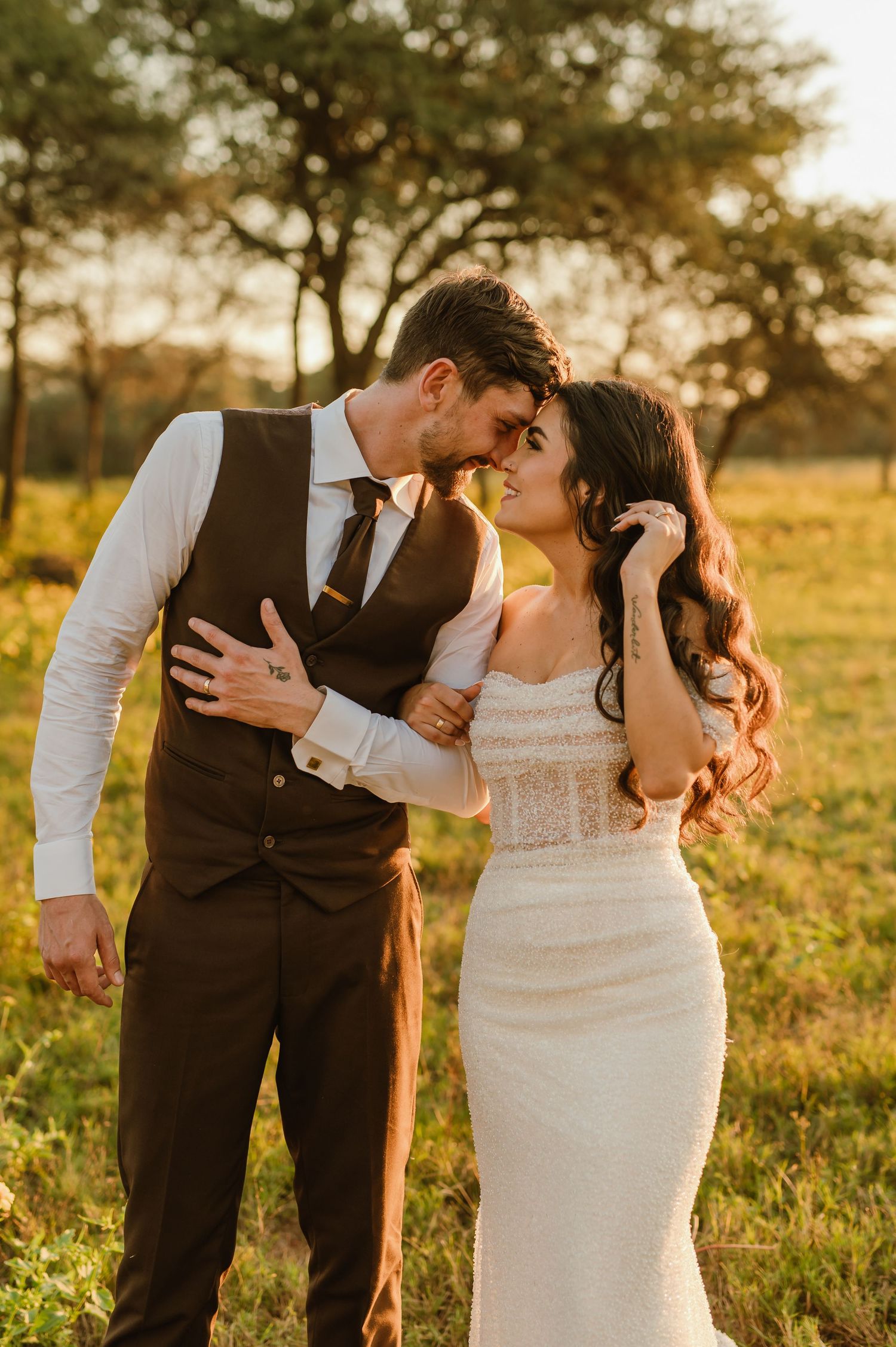 A couple in wedding attire shares romantic moments in a sunlit field during golden hour.