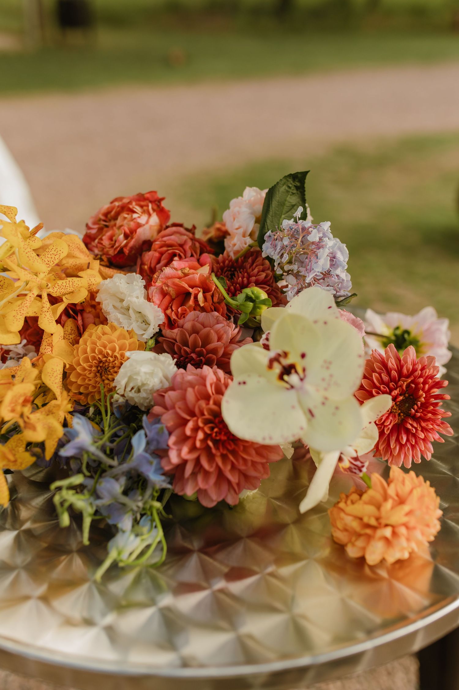 Vibrant wedding bouquet featuring dahlias, orchids, and mixed blooms in orange, pink, yellow, and blue tones.