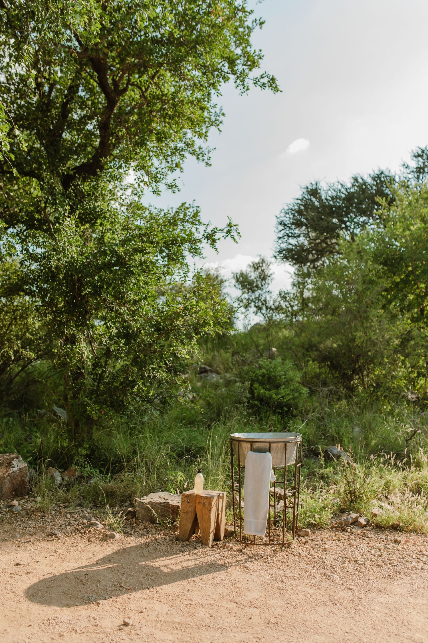 Outdoor hand washing station on a dirt path surrounded by lush green African bush trees.
