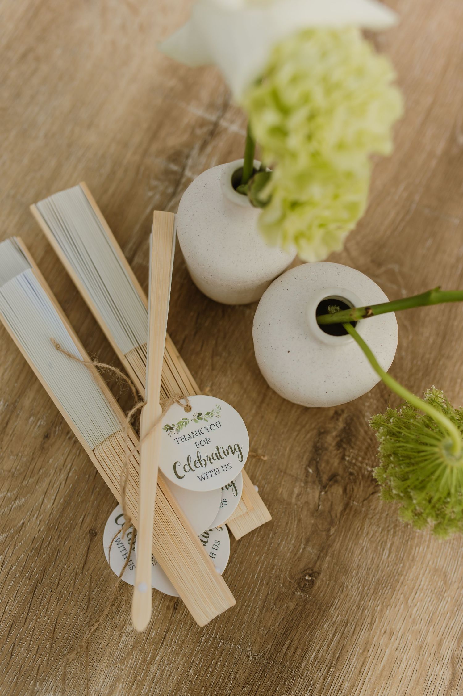 Wedding place cards and small white vases with green flowers arranged on a wooden surface.