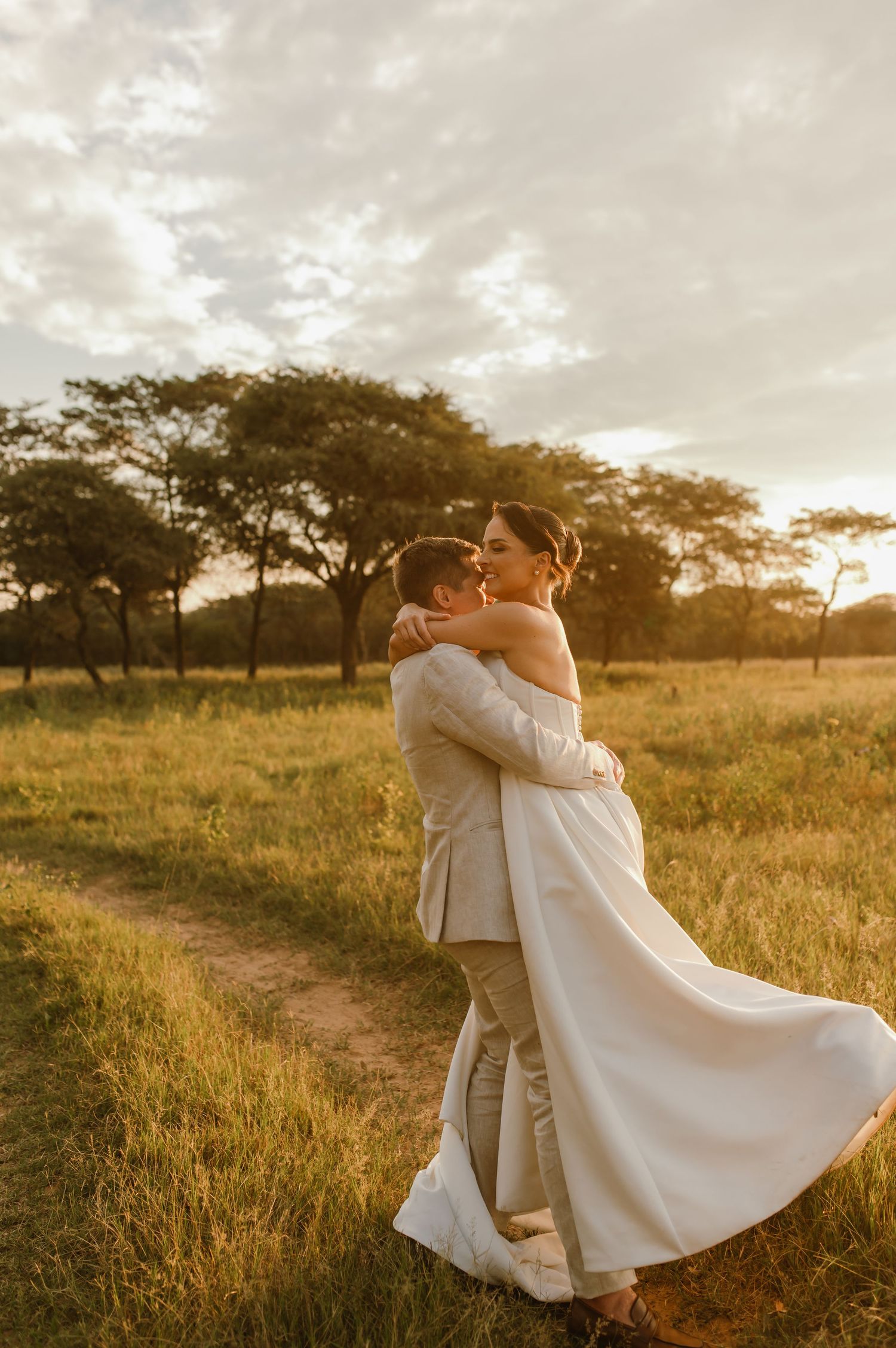 A joyful wedding couple dancing and twirling in a sunlit field during golden hour.