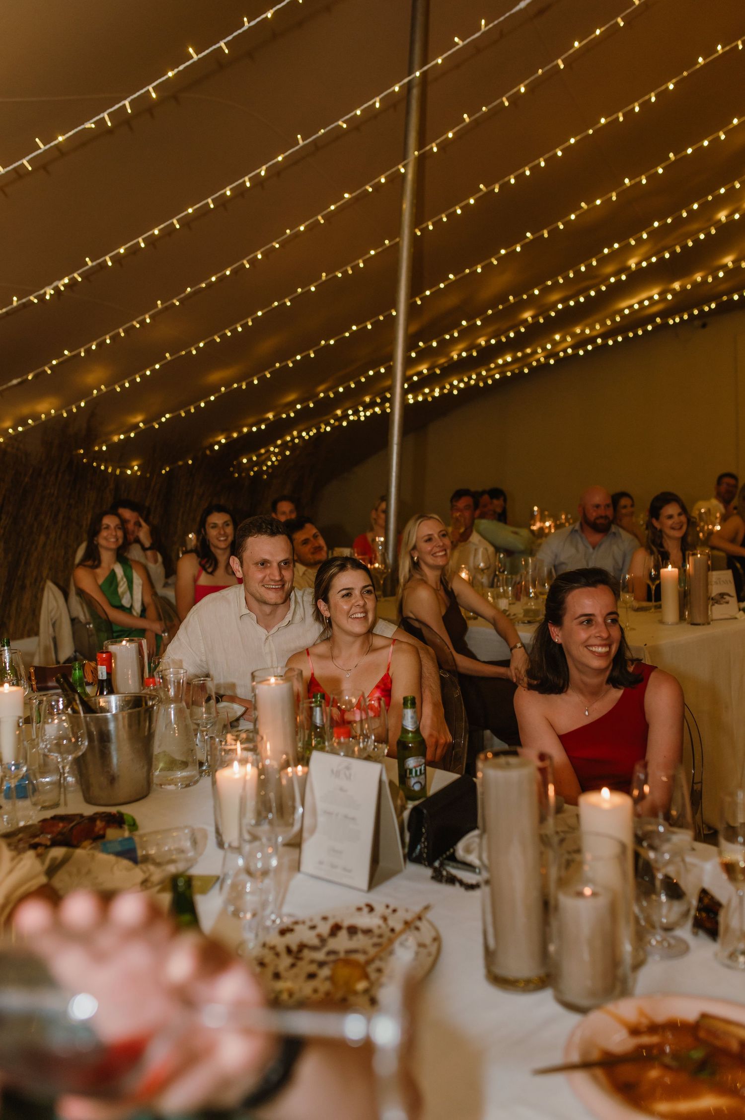Wedding reception guests seated at long tables under romantic string lights during an evening celebration.