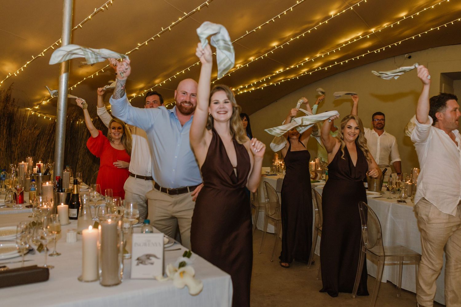 Wedding reception guests dancing and celebrating under warm string lights in an elegant indoor venue.