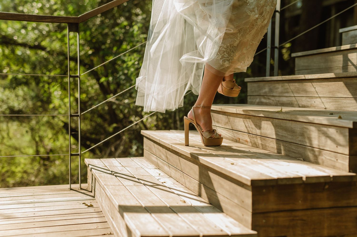 Close-up of a woman in a white dress climbing wooden stairs in high heels outdoors.