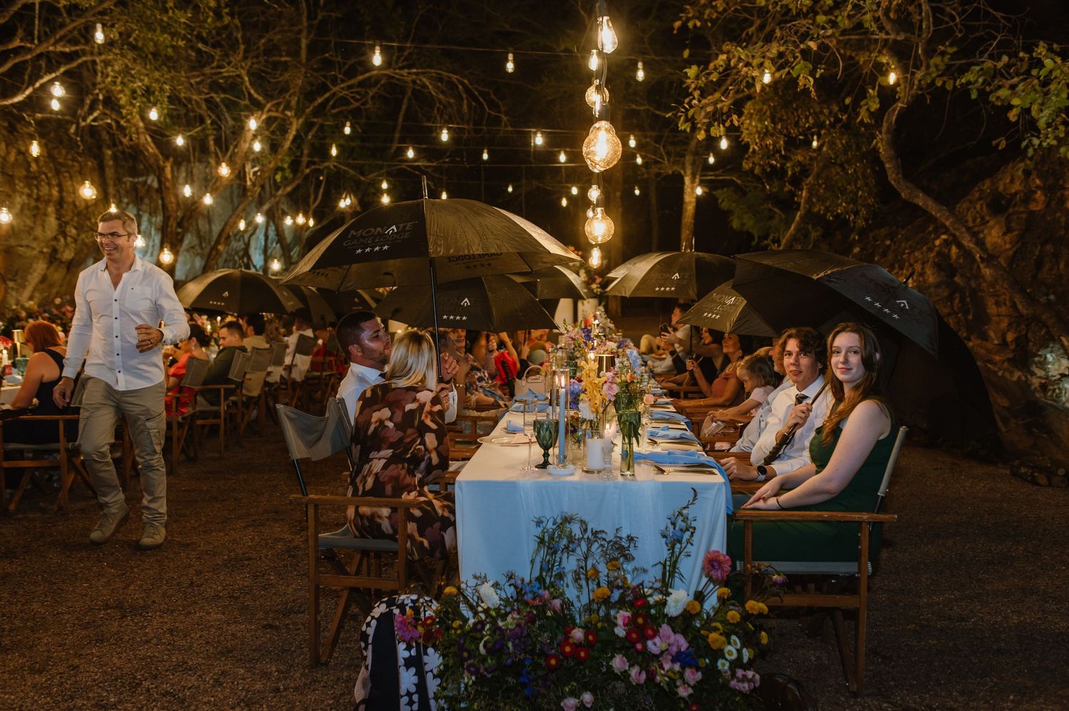 Guests dine under string lights at an elegant outdoor wedding reception at night.