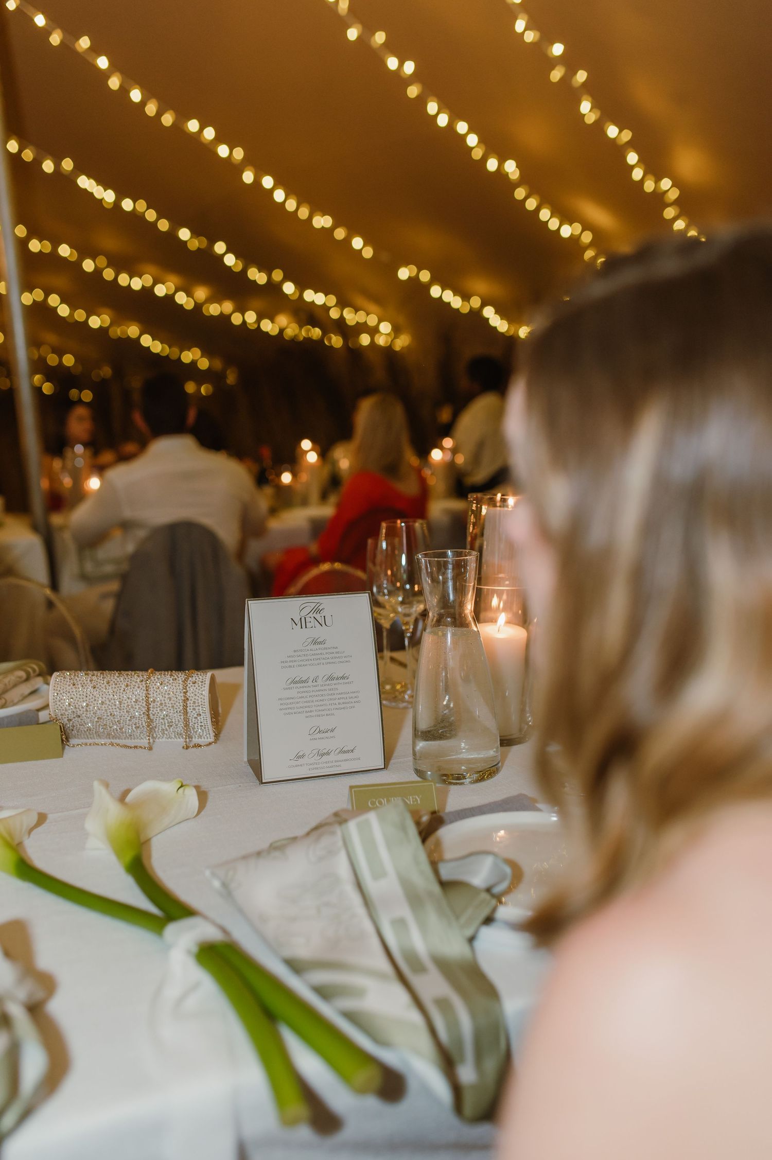 Wedding reception table setting with string lights overhead, menu card, and elegant place settings.