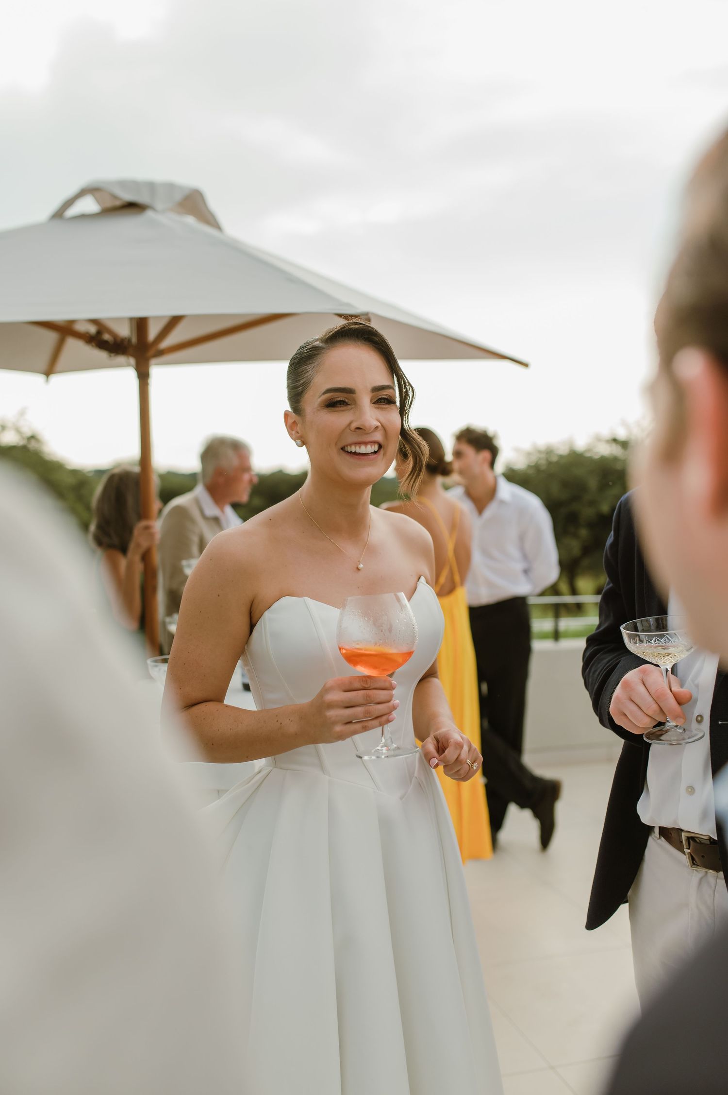 Wedding celebration on a patio with guests mingling under umbrellas at an outdoor venue.