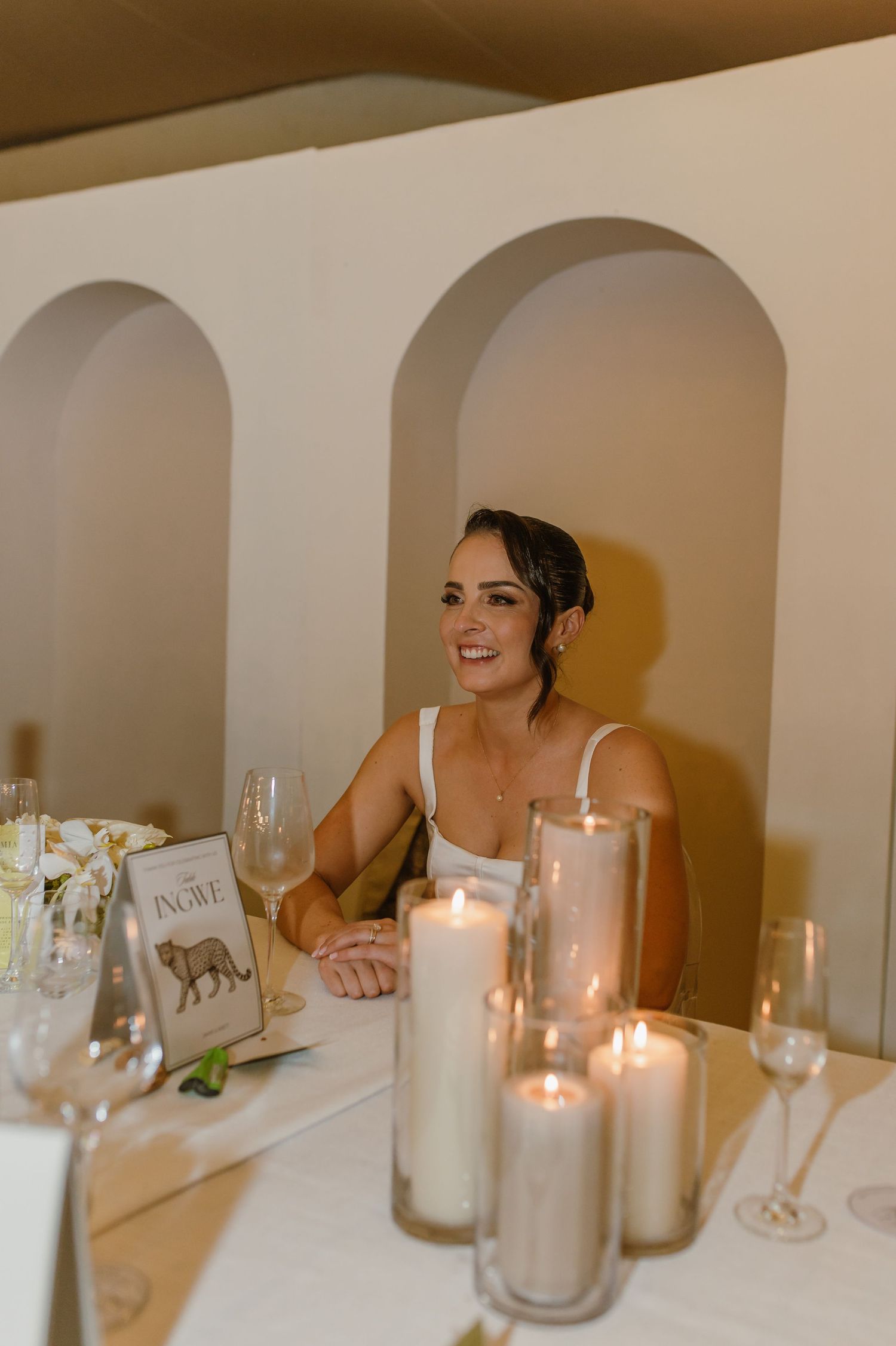 Candlelit wedding reception table with white decor and arched wall details.