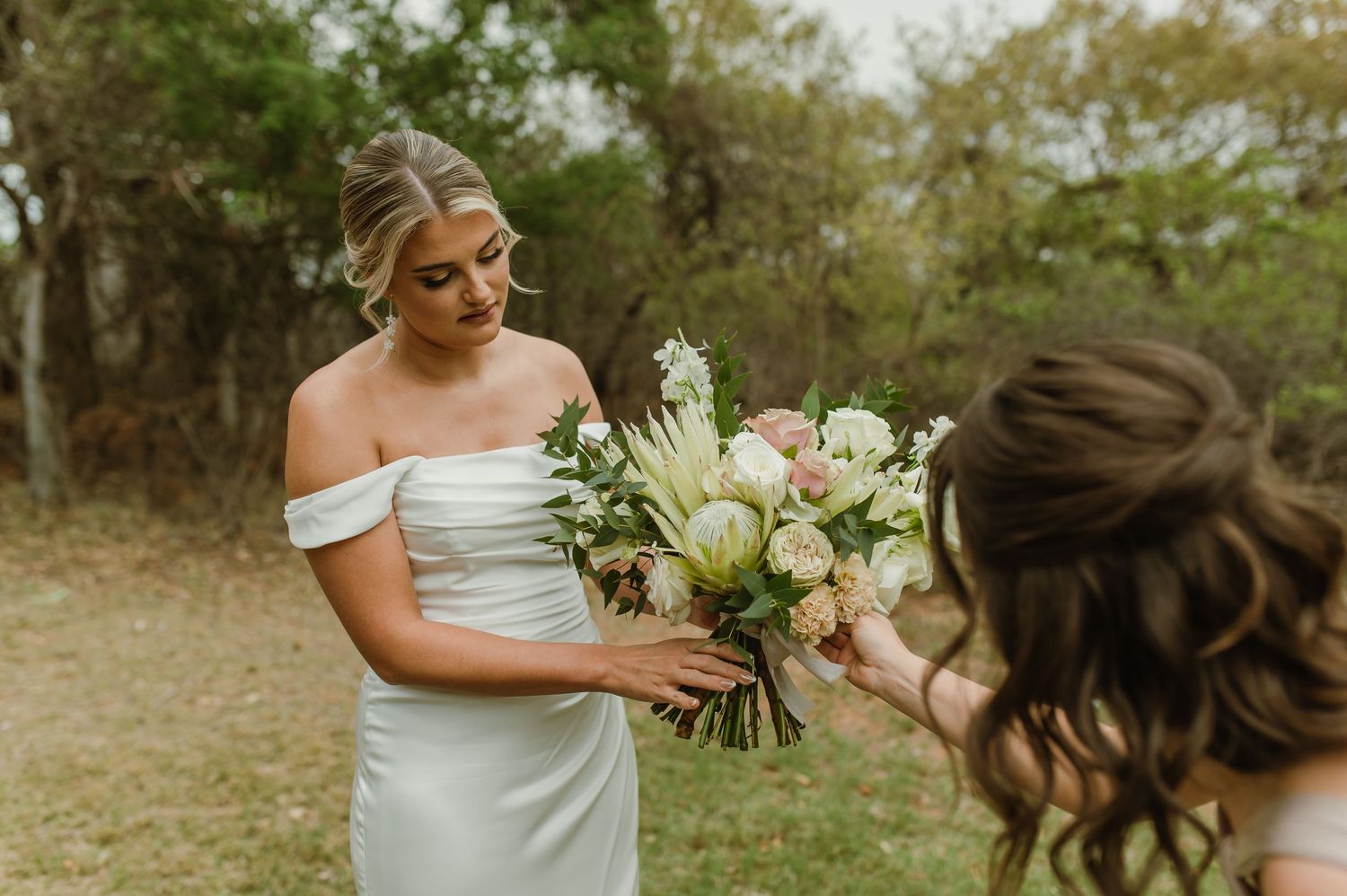 Bridal moment captured with white bouquet handoff in outdoor setting.