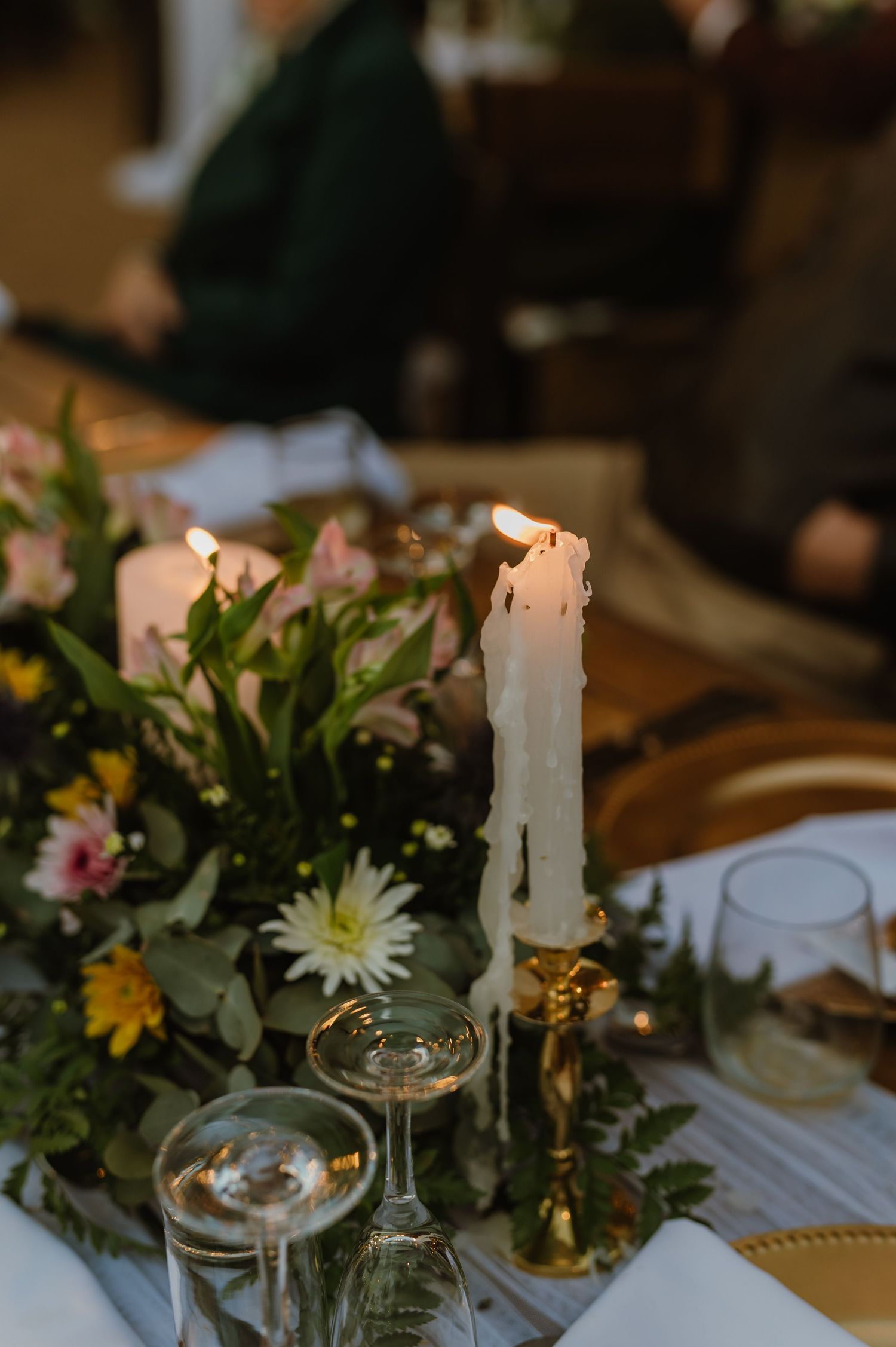 Elegant table setting with white candles, floral centerpieces and glassware for a wedding reception.