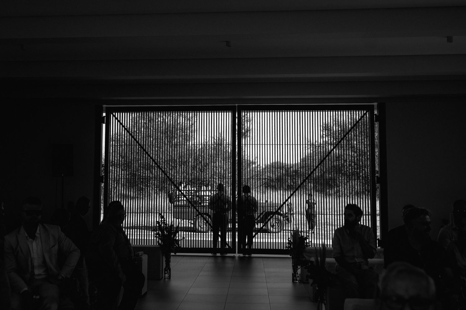 Silhouetted view of wedding ceremony through large windows with dramatic lighting.