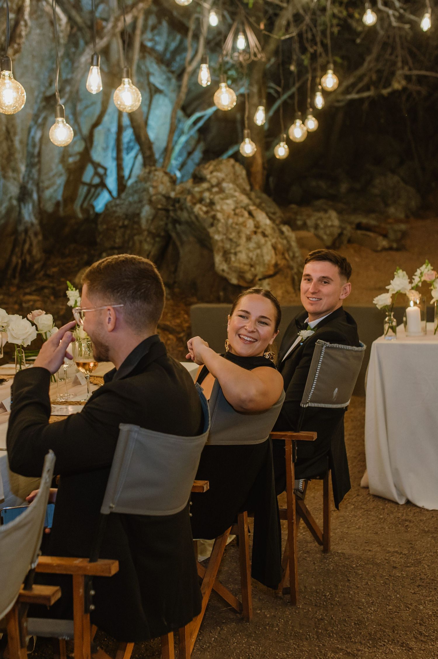 Wedding reception guests enjoying dinner under string lights at outdoor venue.