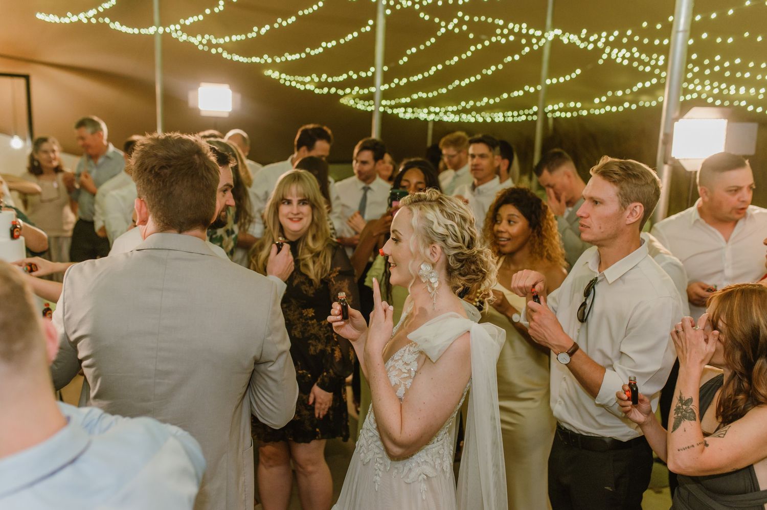 Lively wedding reception dance party under string lights with guests celebrating.