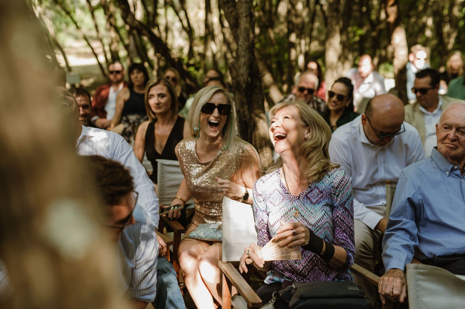 Wedding guests seated outdoors in a natural wooded setting during a ceremony.