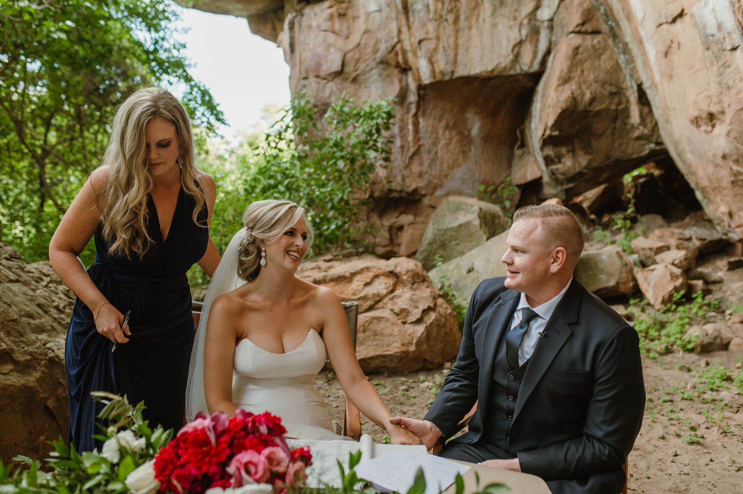 Wedding ceremony setup in a natural cave setting with rustic wooden chairs and floral decorations.