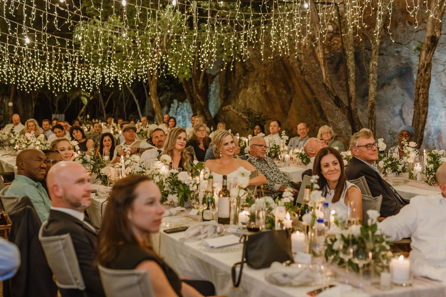 Elegant wedding reception setup with long tables decorated with greenery and candles under string lights.
