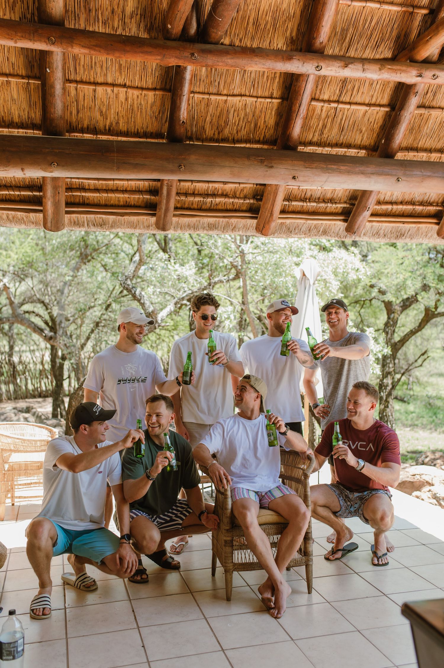Group of friends lounging on chairs under thatched roof pavilion.