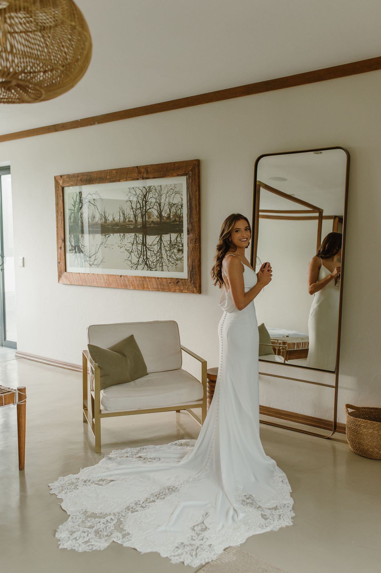 Elegant white wedding gown with lace train photographed in a modern room with mirror and artwork.