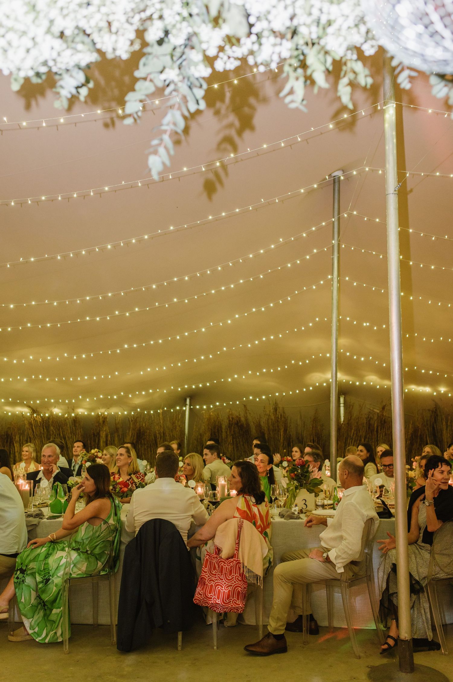 Large wedding tent filled with guests and decorated with string lights creating a magical atmosphere.