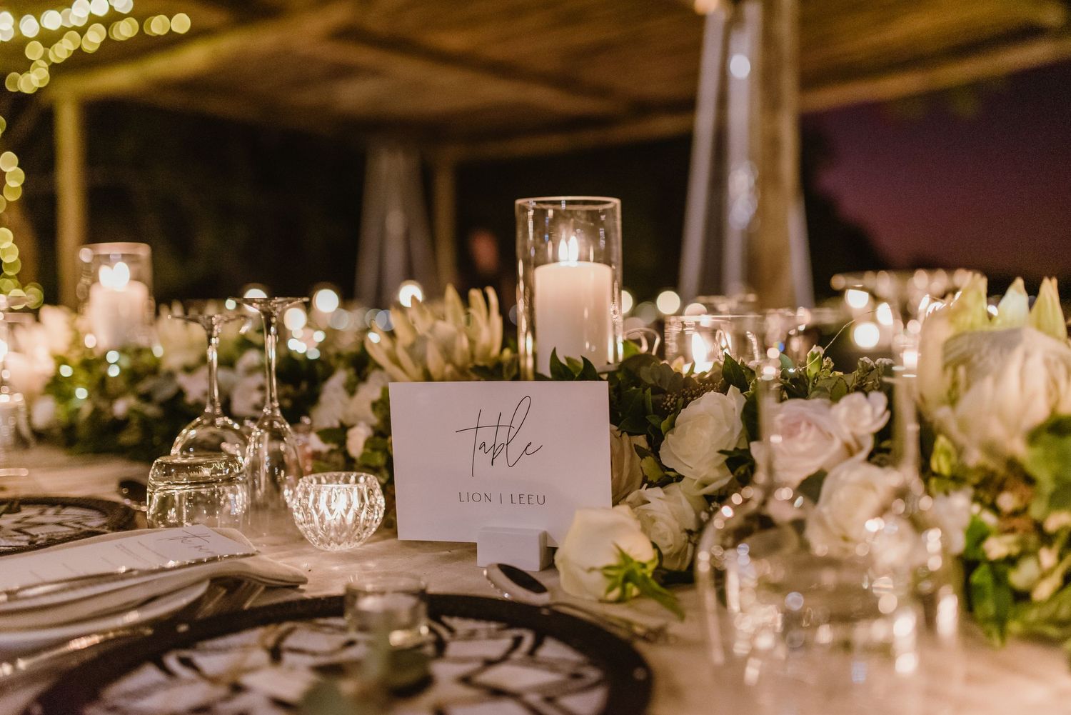Wedding reception table details with black charger plates, white candles and floral arrangements.