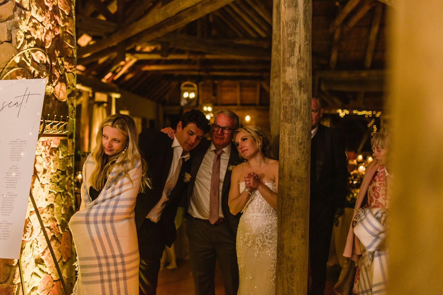 Wedding reception guests gathered in rustic barn venue with warm lighting and decor.