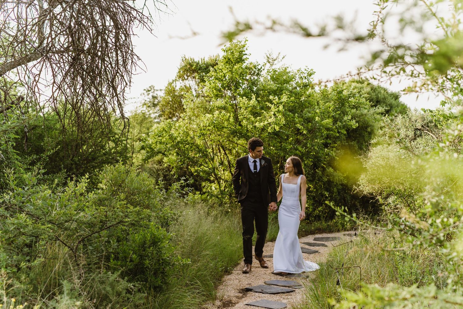 Couple walking together on a stone path surrounded by lush greenery.