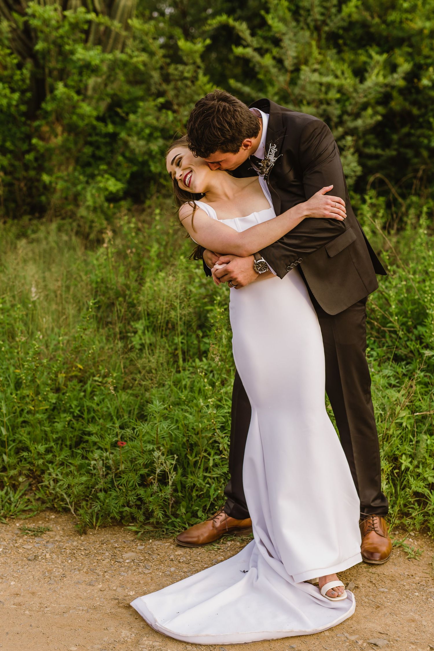 Dramatic dip kiss between newlyweds on desert path with flowing white dress.