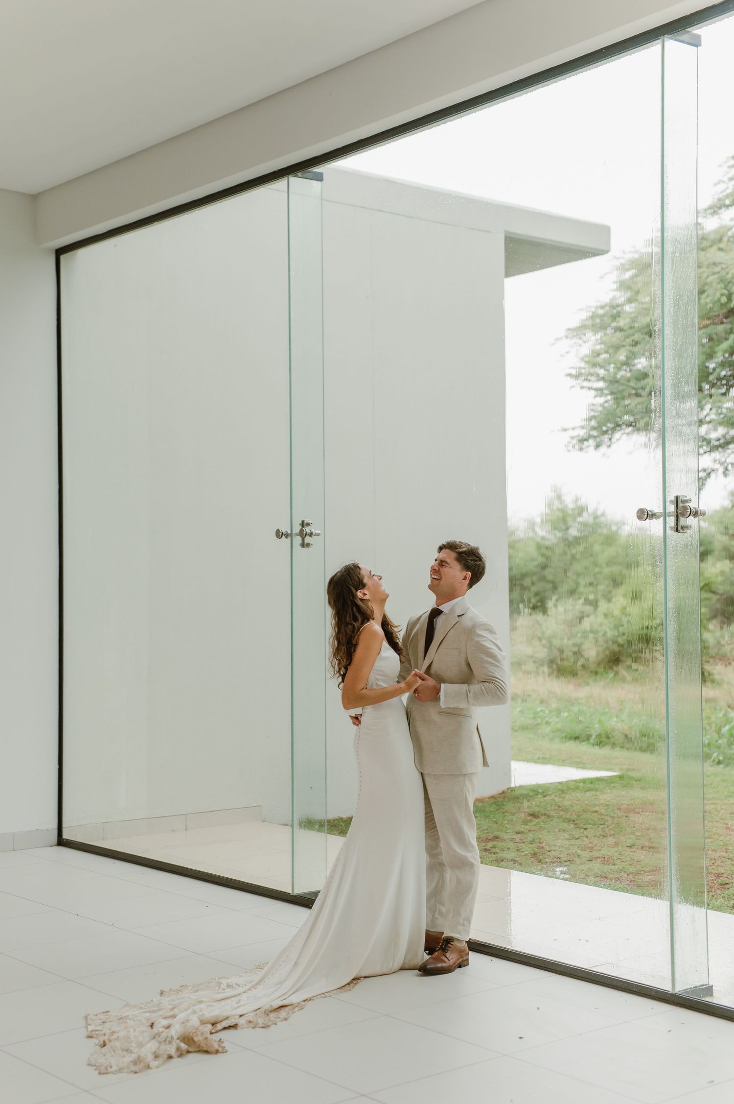 Wedding couple poses in a modern architectural space with large glass windows and natural light.