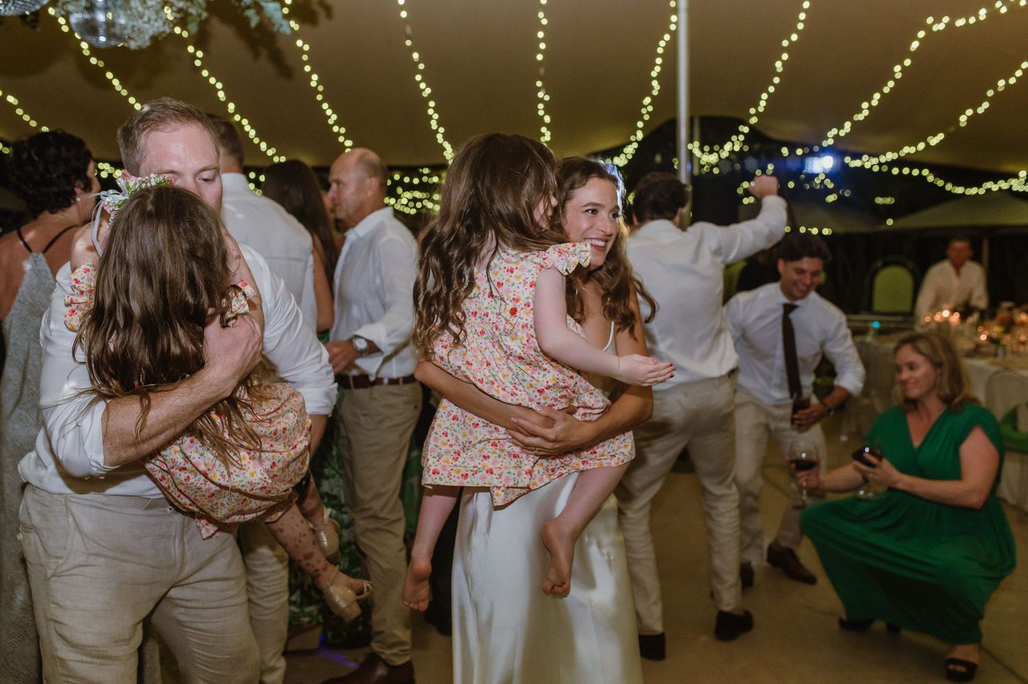 Wedding guests dancing and laughing beneath glowing string light decorations.