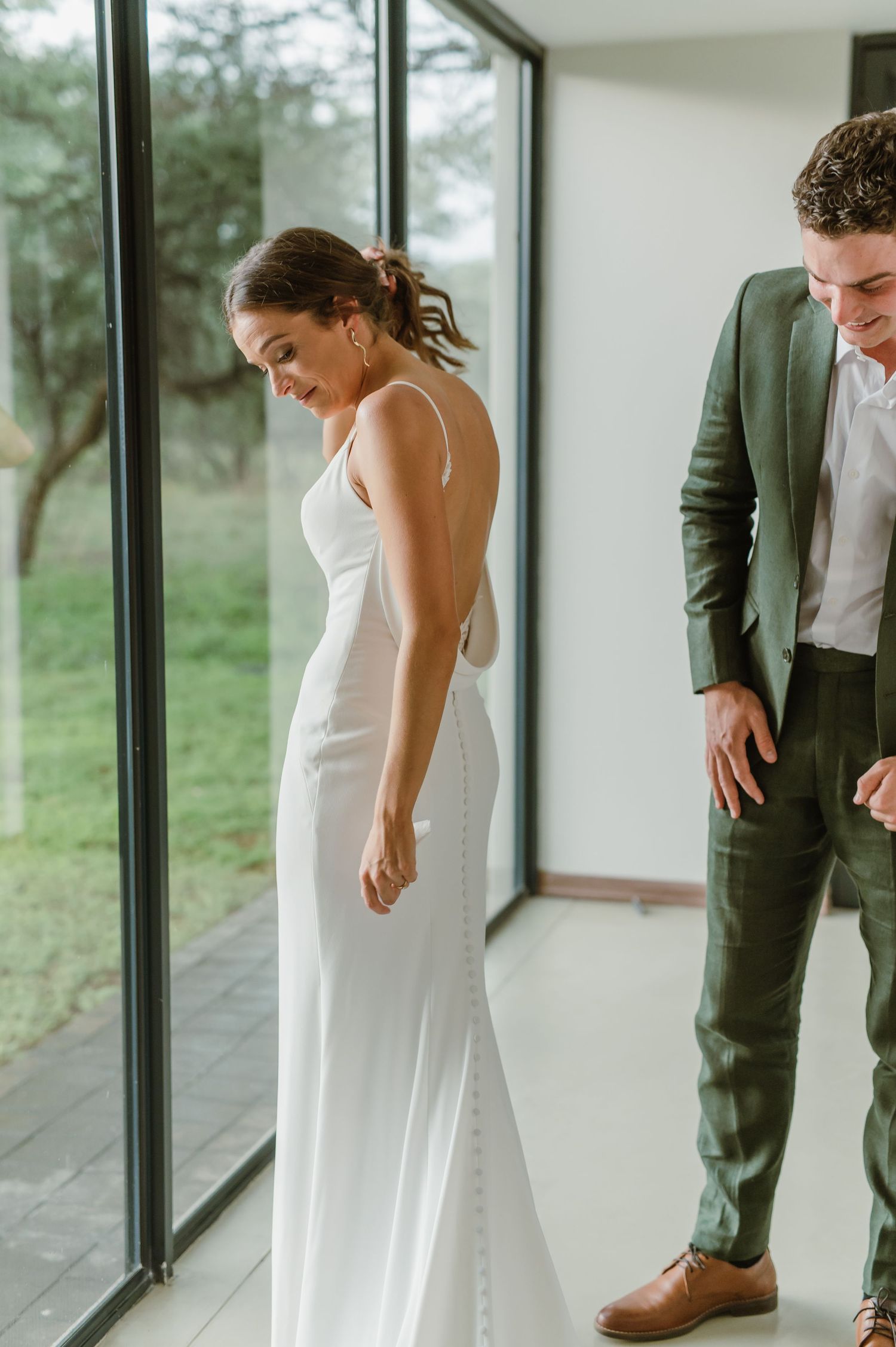 First look wedding photos showing emotional reactions in a modern space with floor-to-ceiling windows.