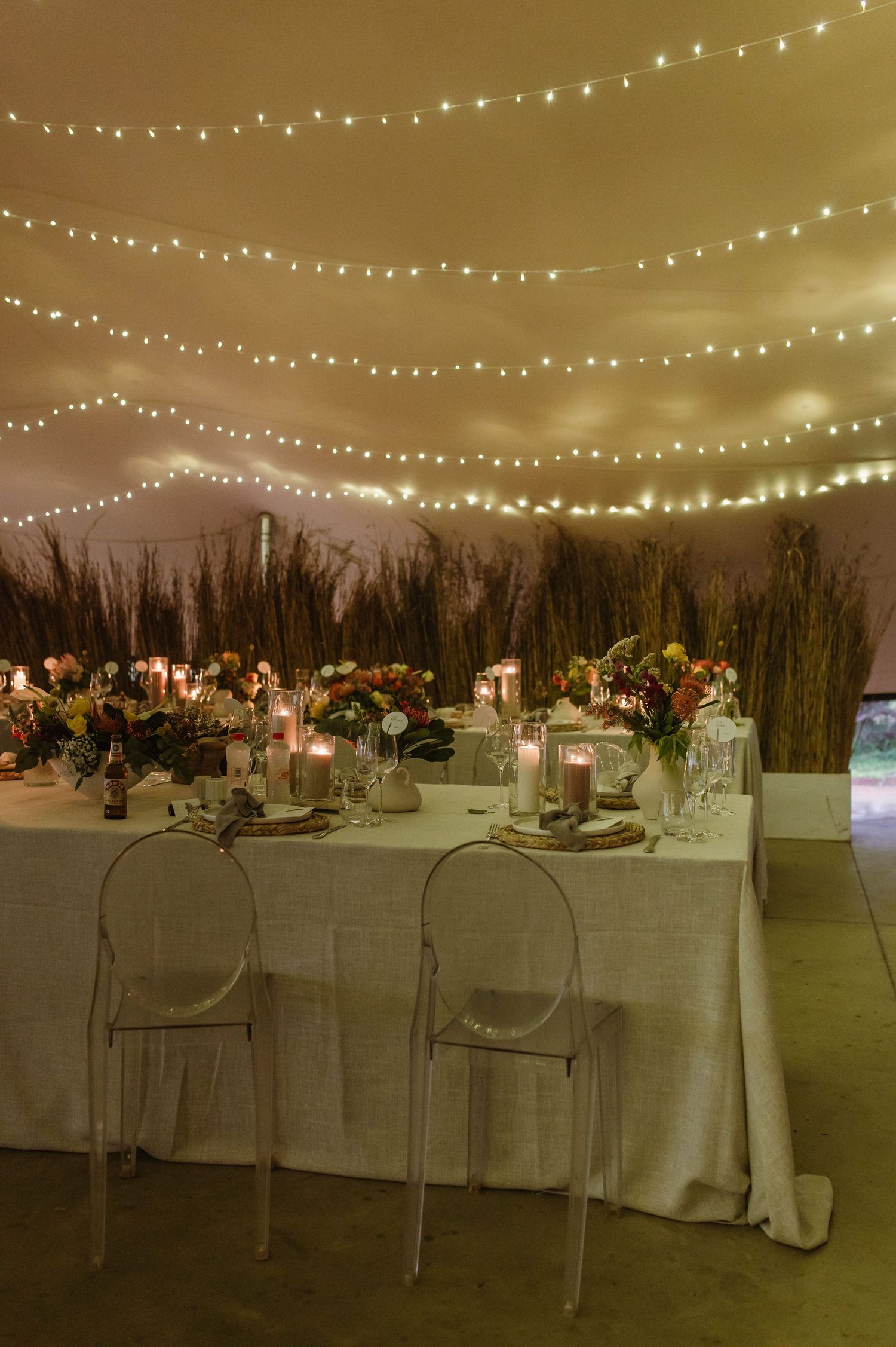 Wedding reception tent with elegant white tablescapes, string lights, and floral arrangements.
