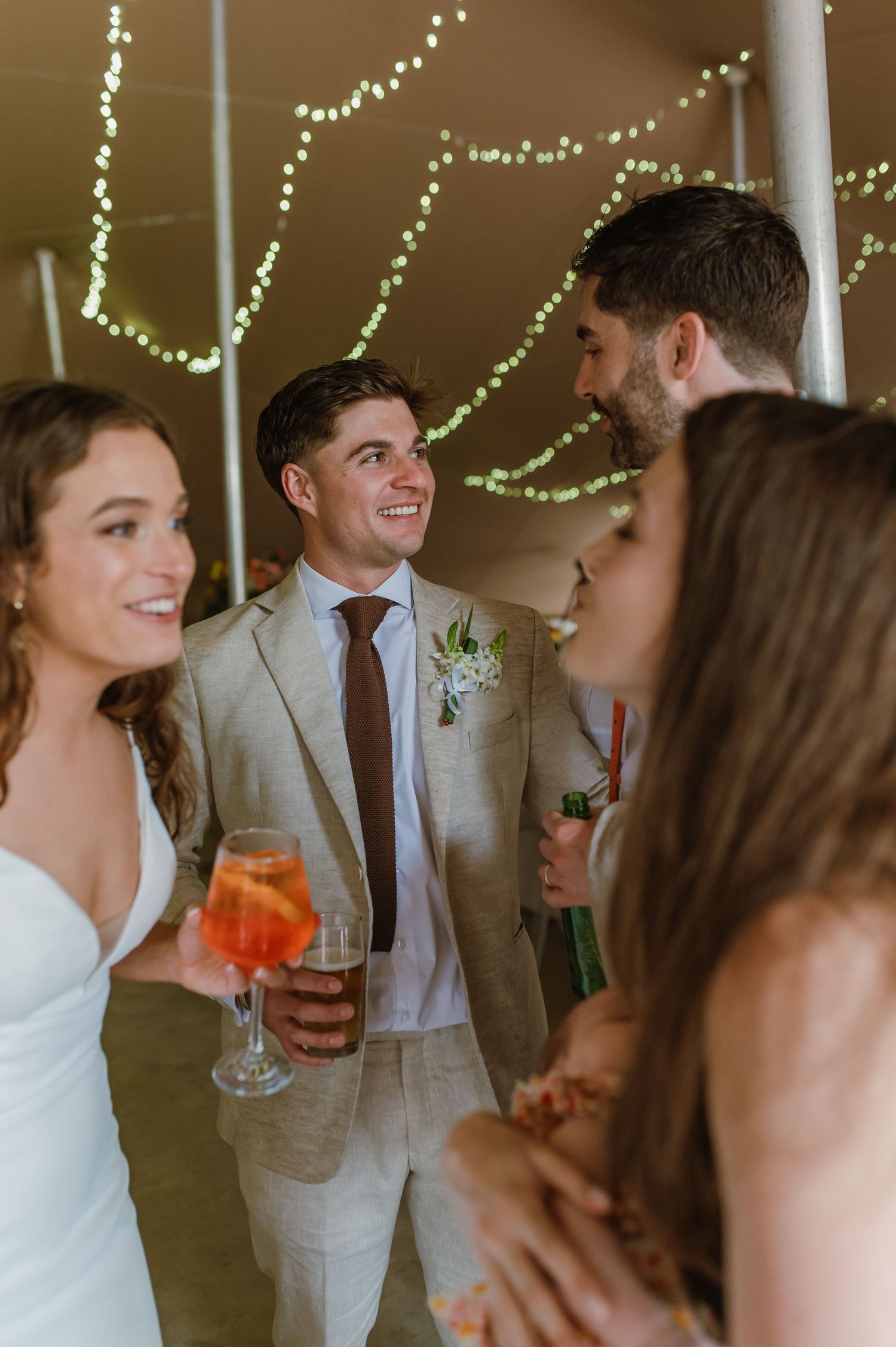Wedding guests in formal attire socializing and enjoying drinks under string lights.