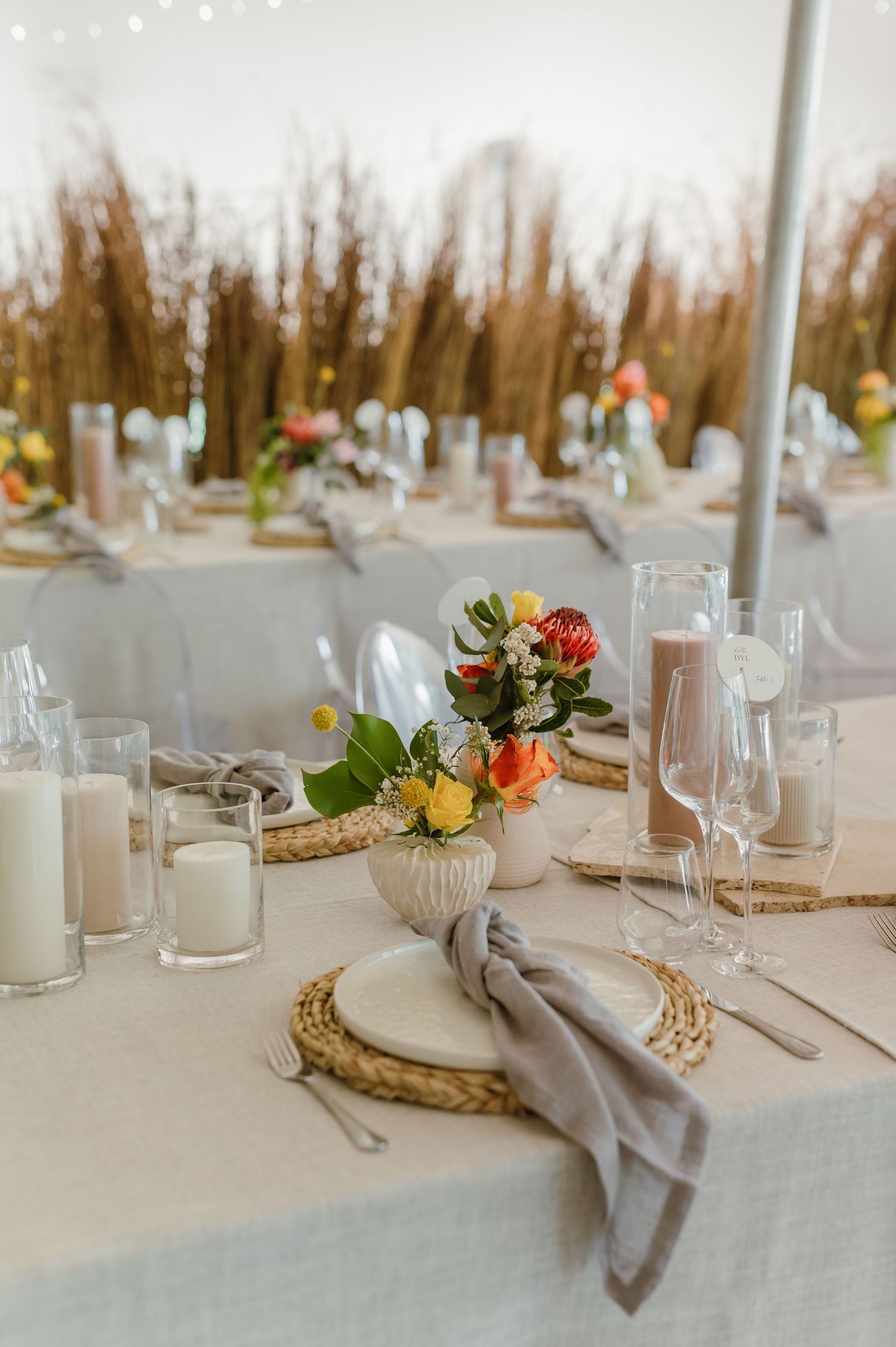 Minimalist wedding table setup with white candles, woven chargers, and fresh floral centerpieces.