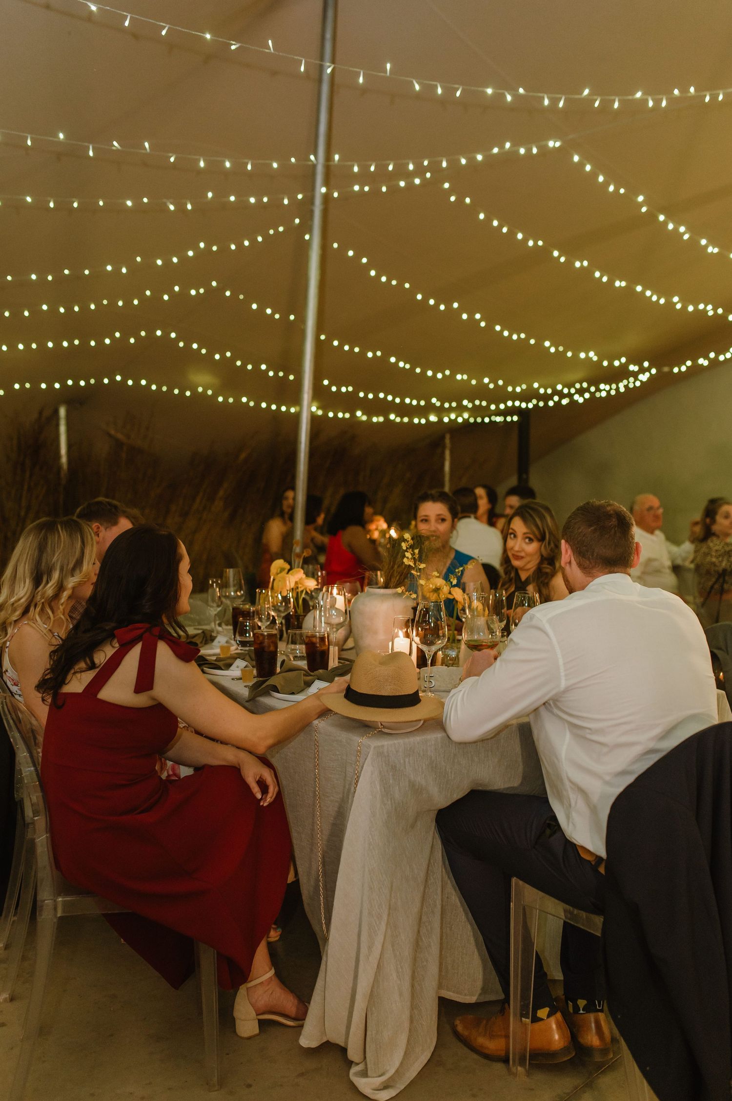 Wedding reception tent with string lights overhead and guests seated at long tables.