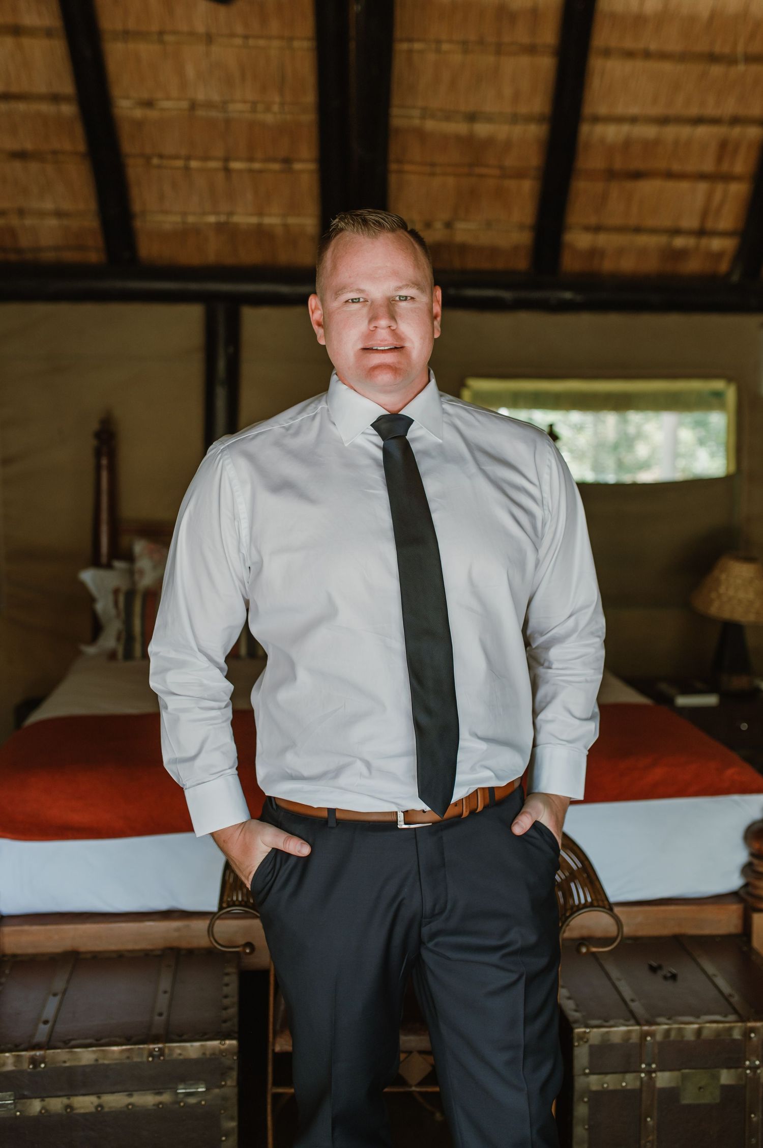 Someone in business attire adjusting their tie in a room with wooden beams and thatched ceiling.