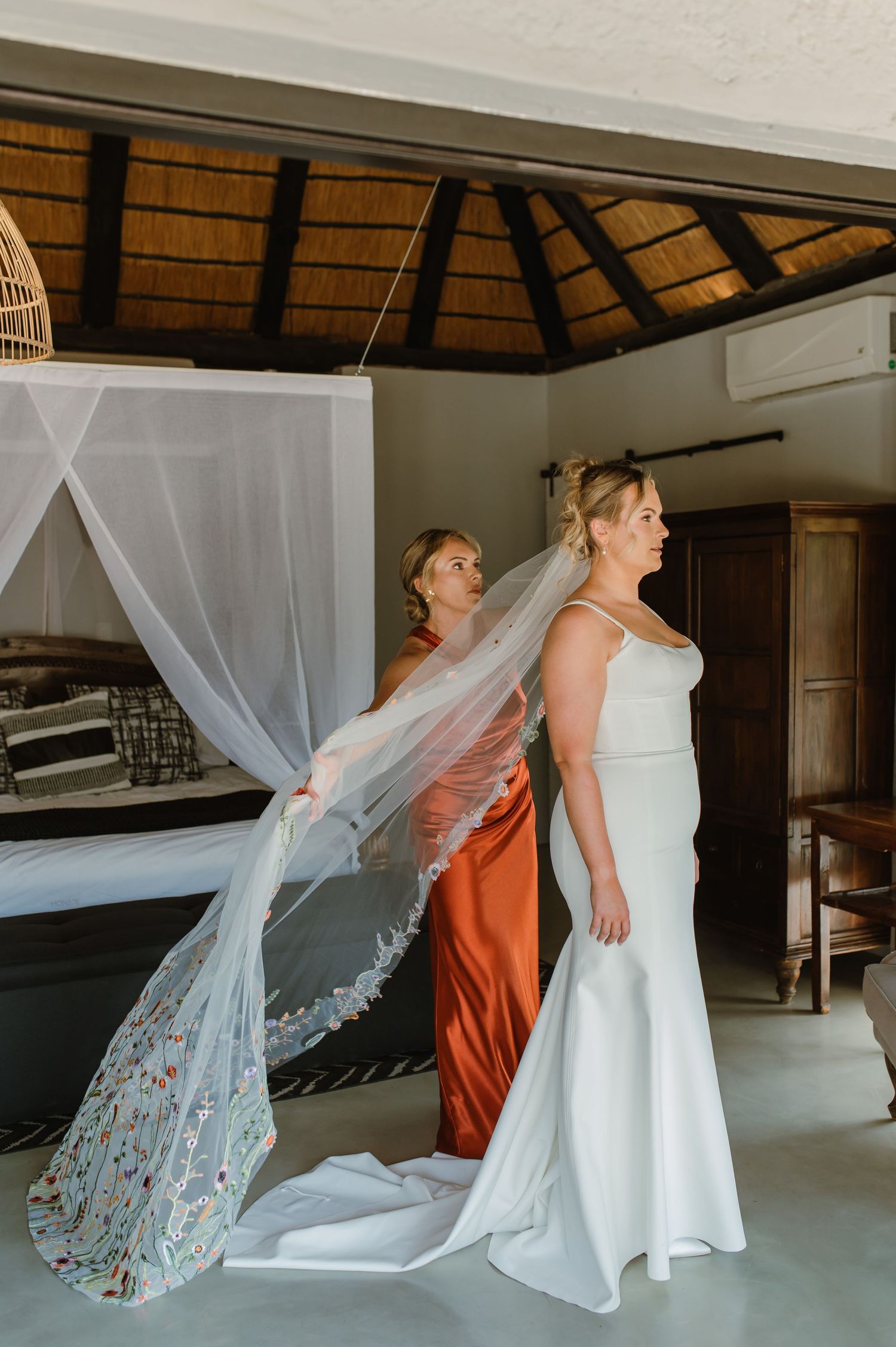 Wedding dress and veil preparation with bridesmaid in burnt orange dress helping.