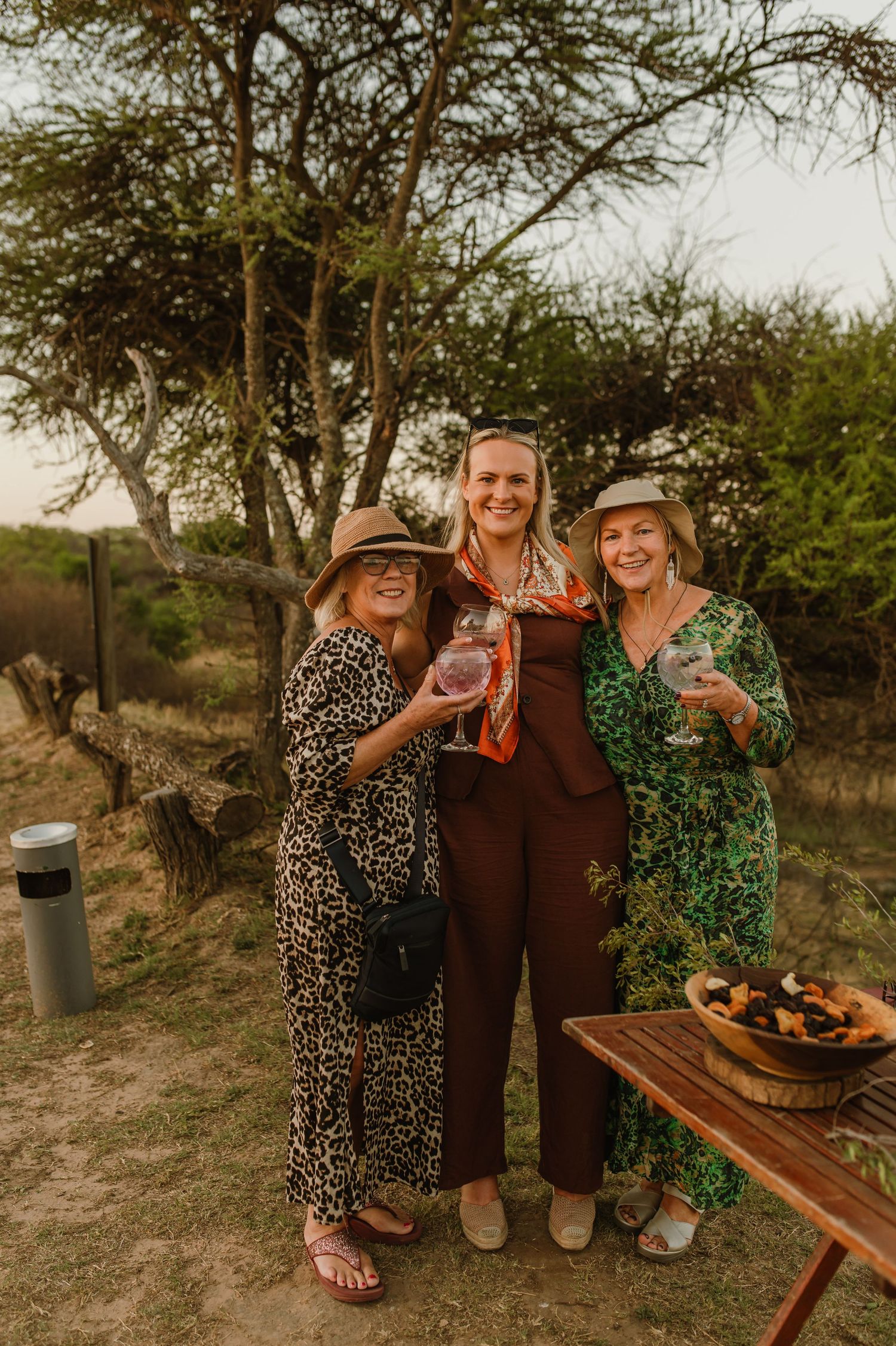 Friends gathered outdoors for drinks and snacks at a rustic wooden table during golden hour.