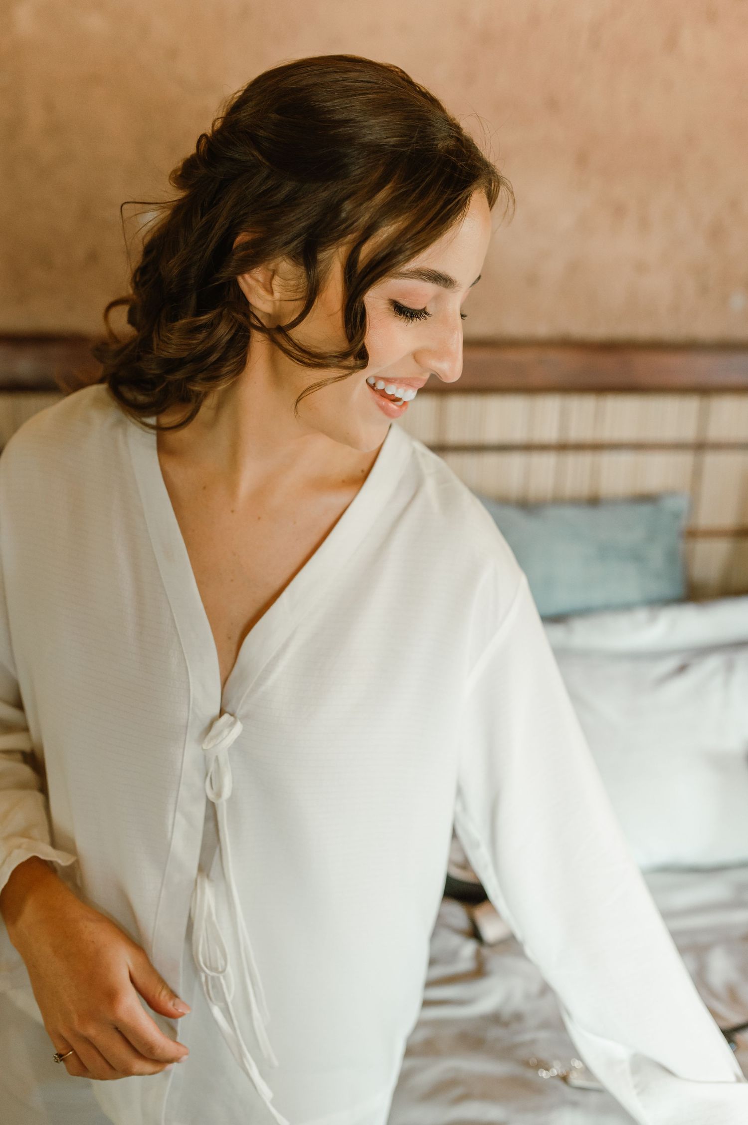Someone wearing a white robe sits on a bed in soft morning light.