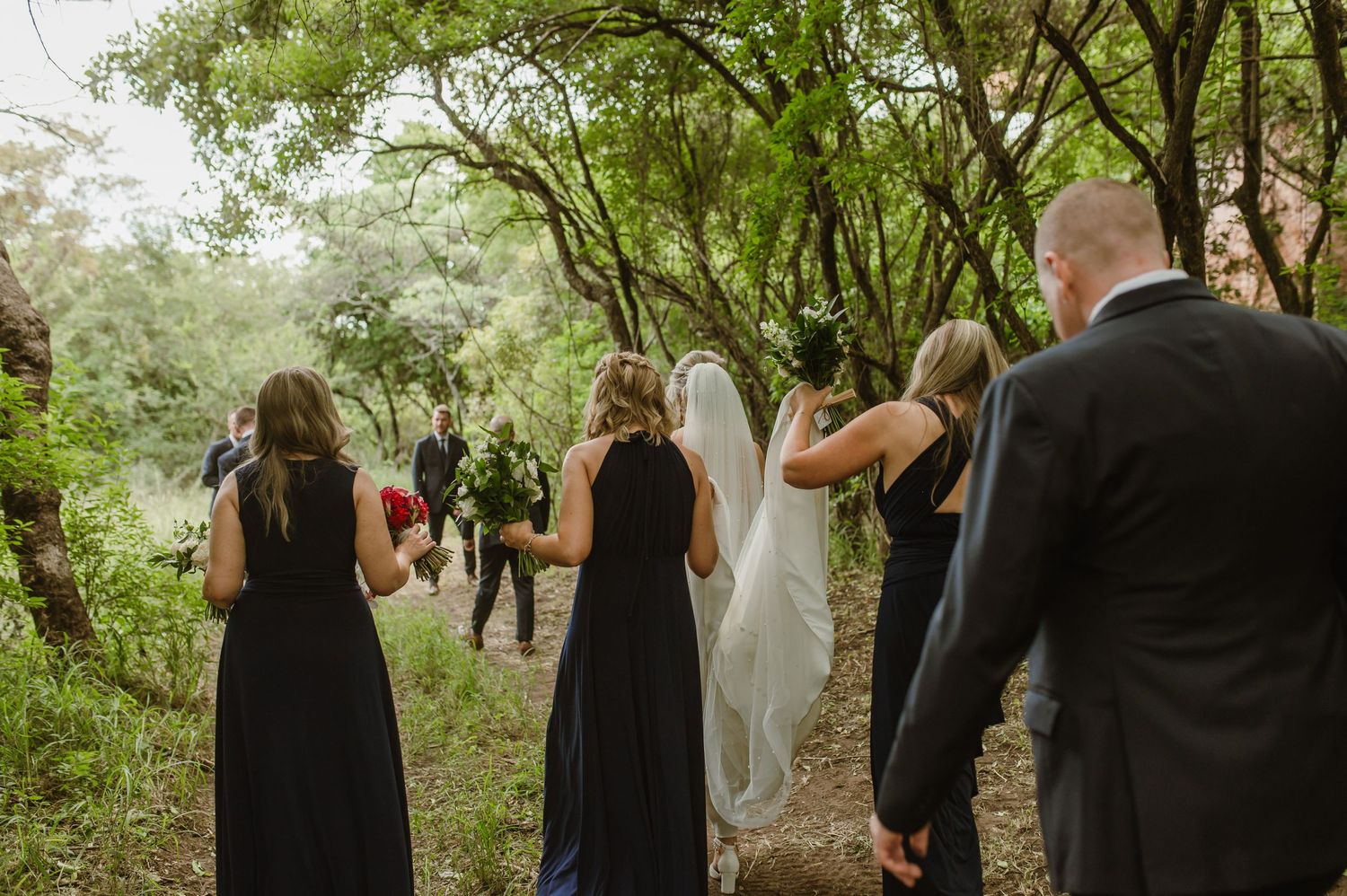 A wedding party walks along a tree-lined path during an outdoor ceremony.