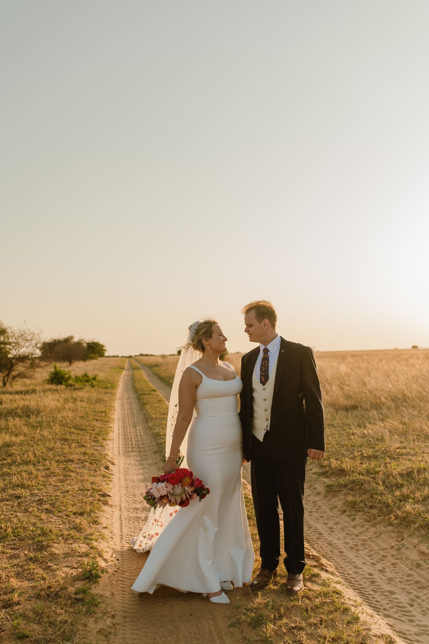 A couple shares a tender moment on a rustic path during their sunset wedding photoshoot.