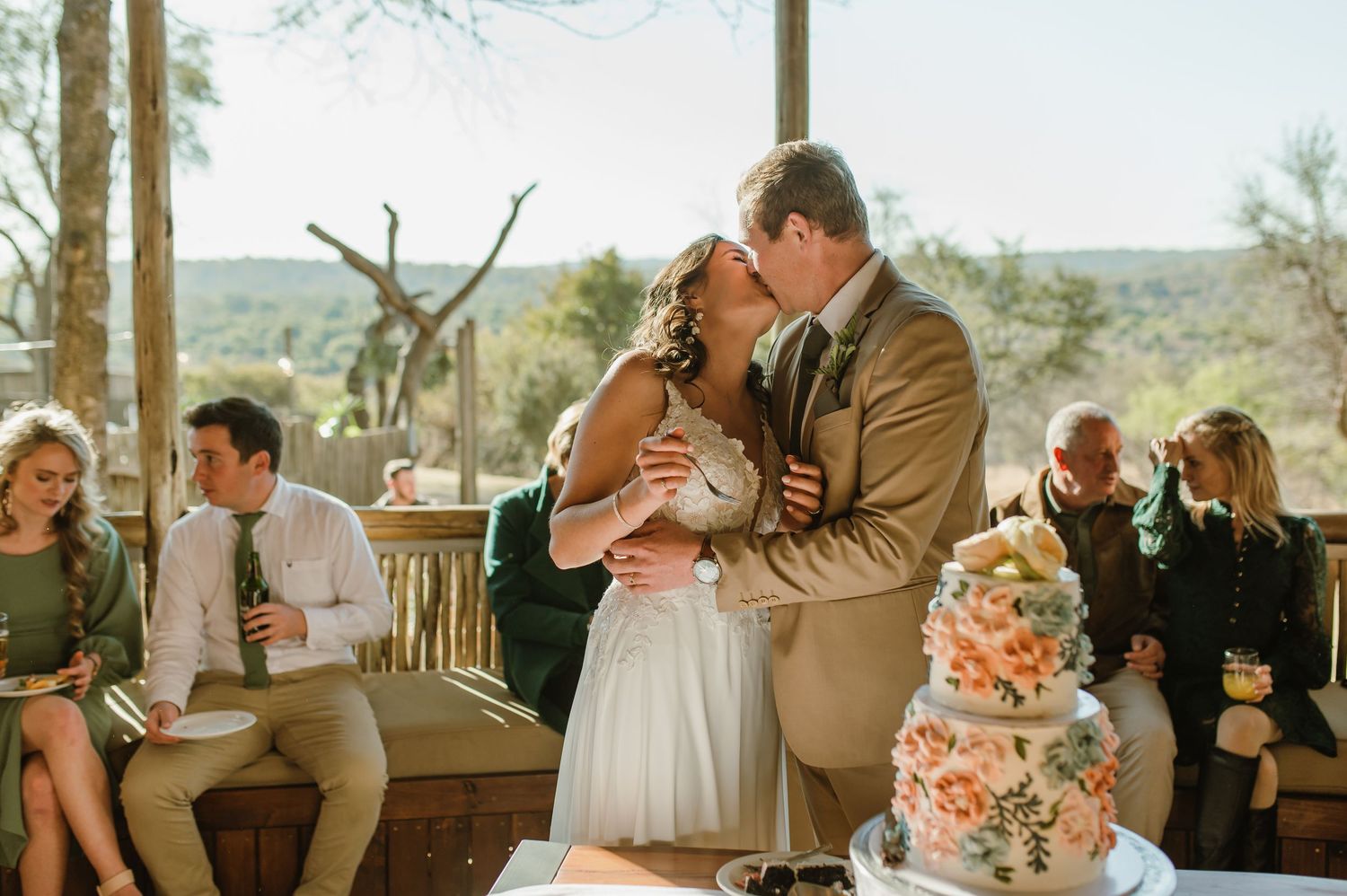 Outdoor wedding celebration with tiered floral cake on rustic wooden deck.